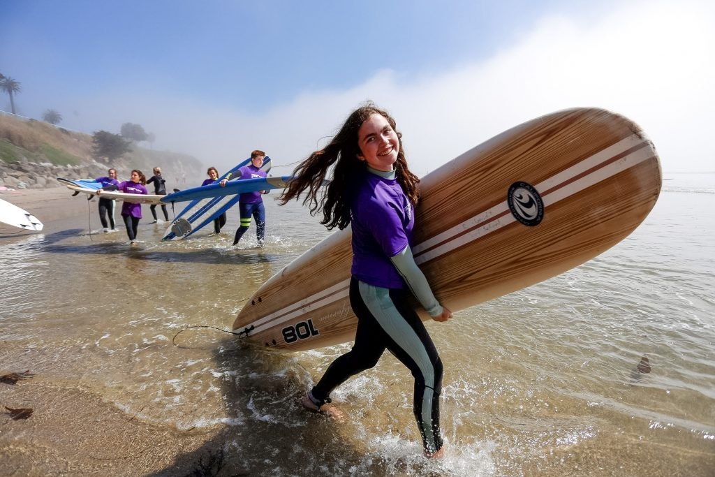 A group of teen travelers holding surf boards about to go surfing on a beach in California.