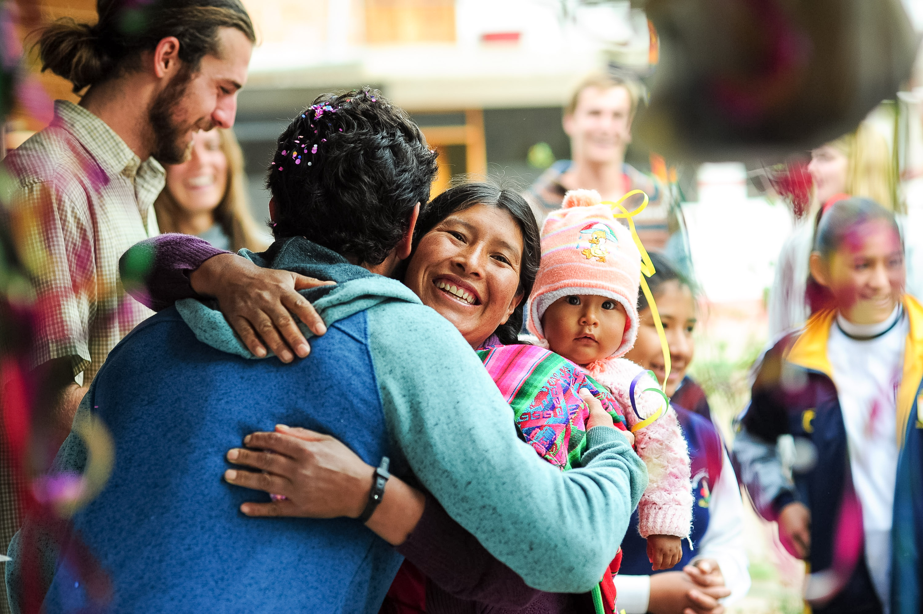 A local woman carrying a baby embraces a student during a community greeting