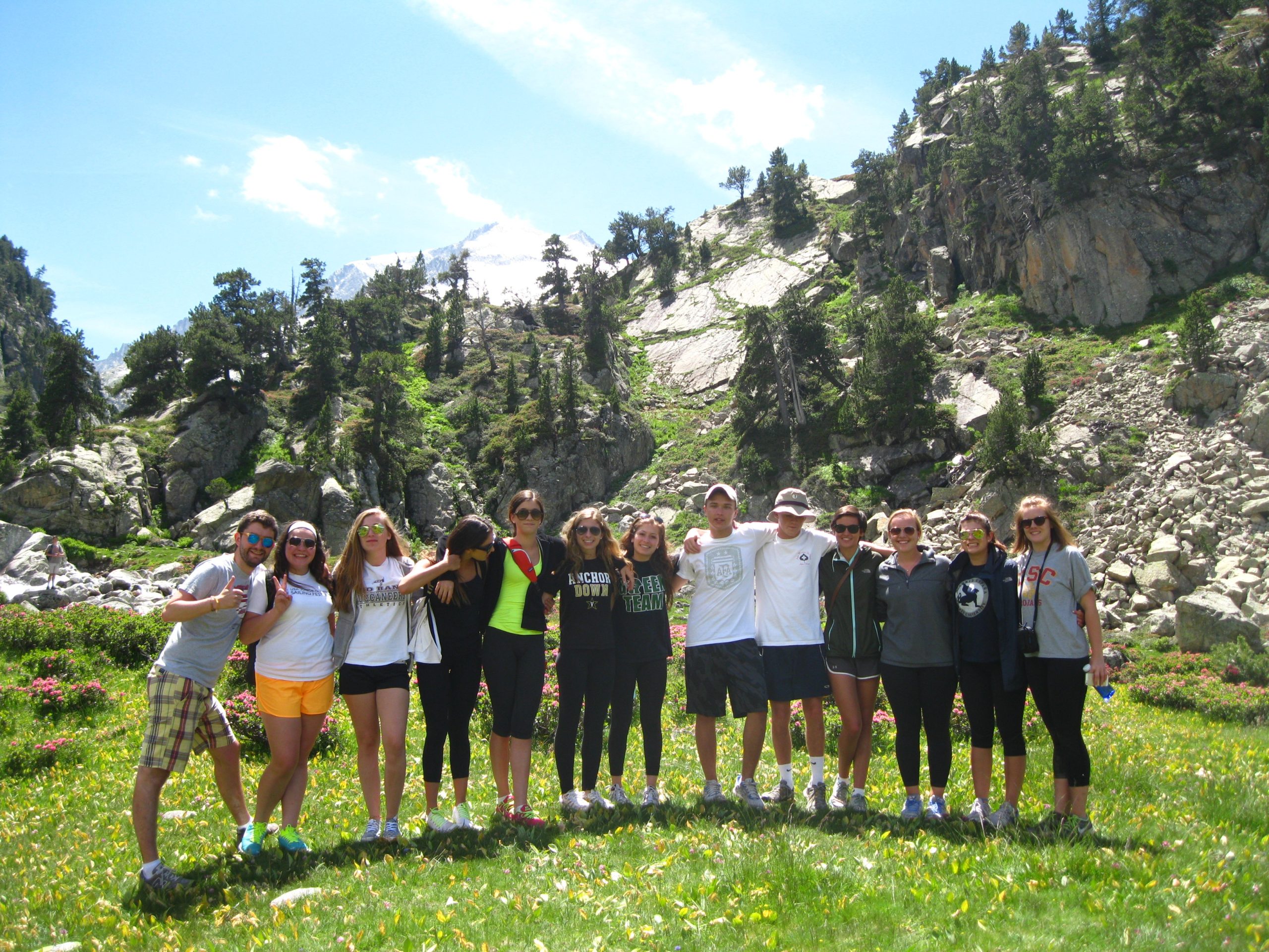 Teens pose together in a mountain meadow with cliffs and pine forest behind them