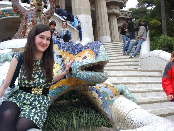 A girl sits next to a mosaic covered lizard statue in Park Guell in Barcelona