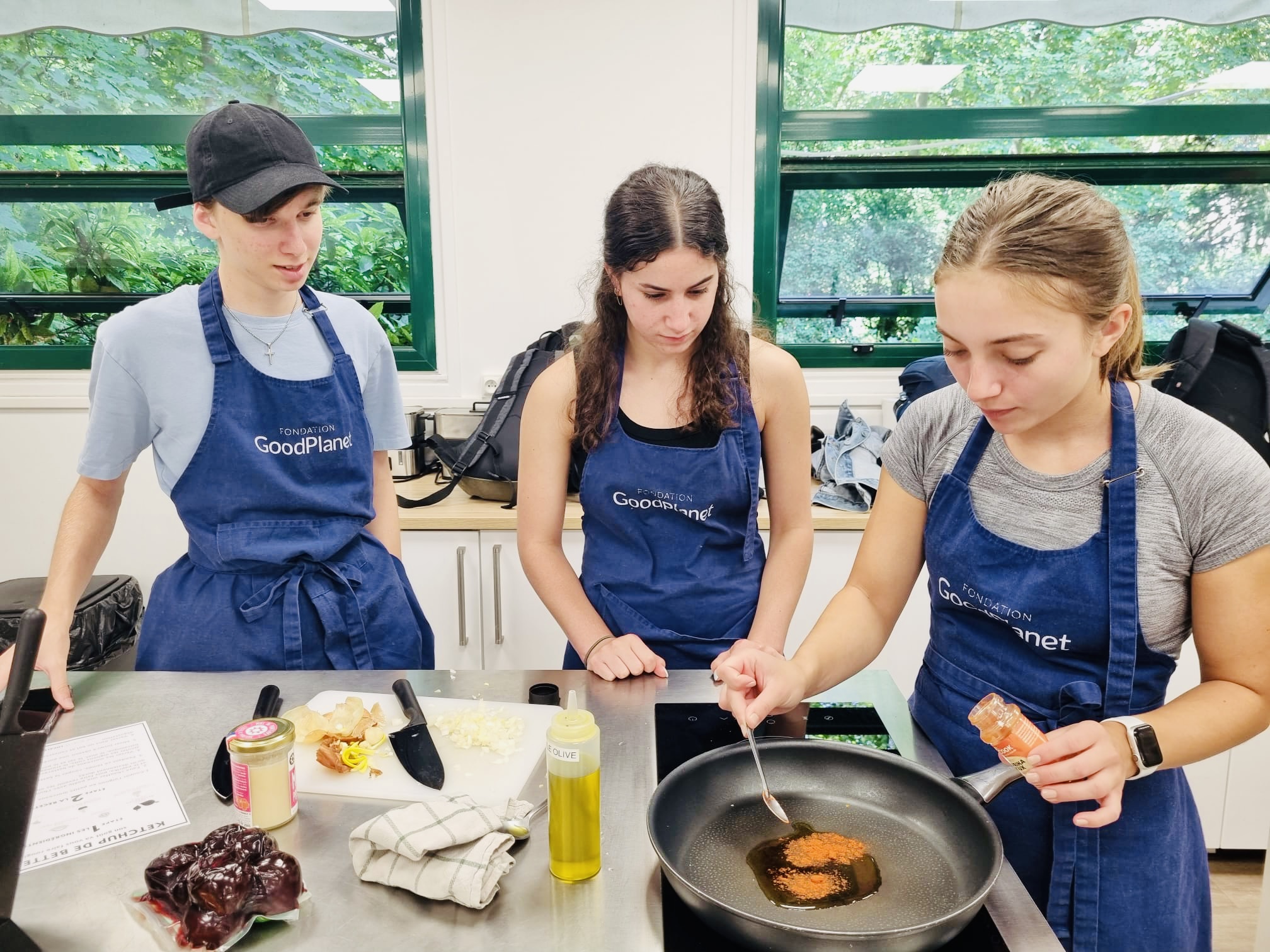 Three students prepare food together during a supervised cooking activity.