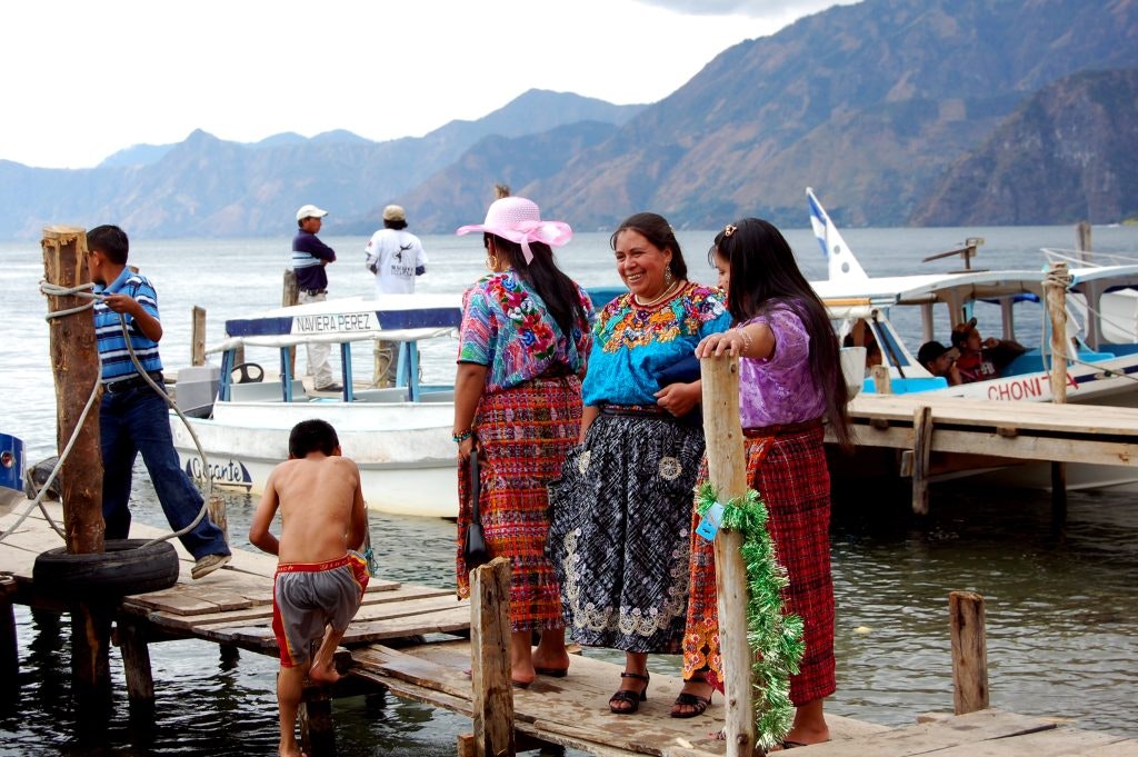 Women in traditional clothing in Guatemala stand next to a lake.