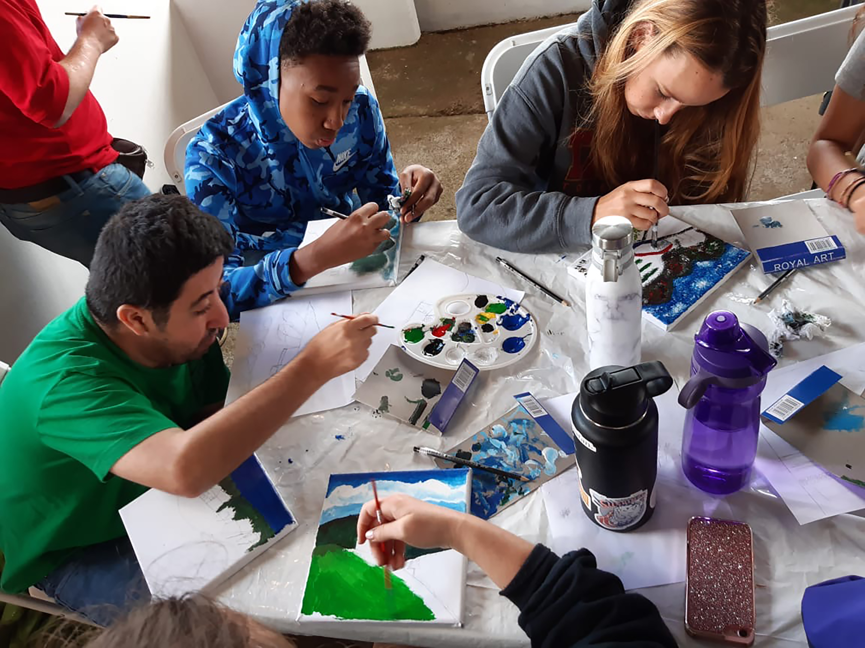 Students sit together at a table and paint during a group art activity.