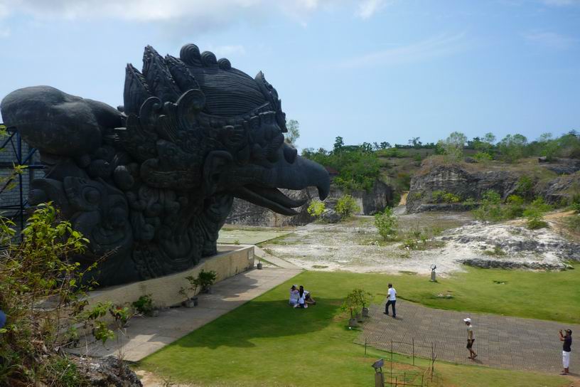 A large carved dragon statue overlooks a grassy park where visitors walk and take photos