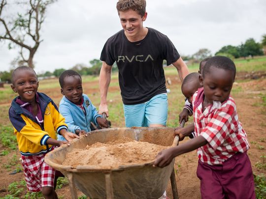 A student and local children push a wheelbarrow full of sand together