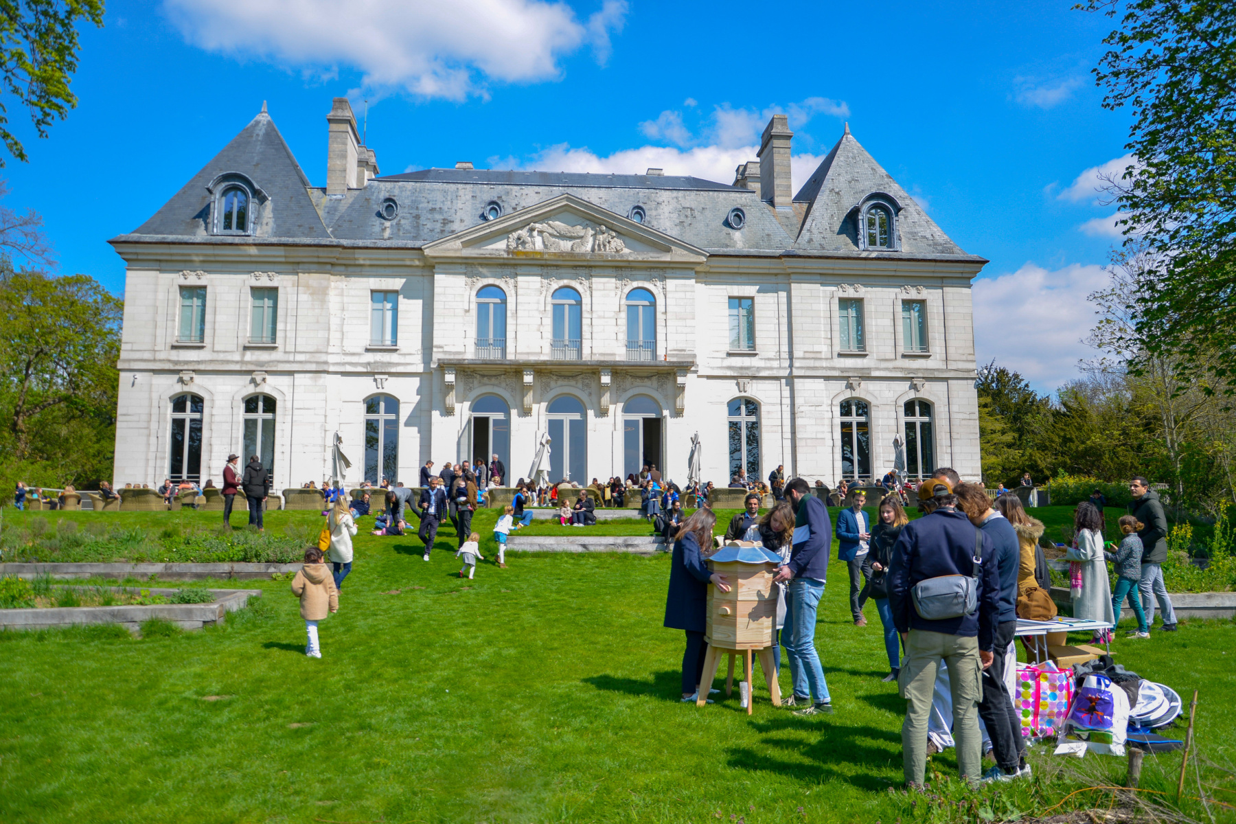 A grand white château with people painting outside on a sunny day.