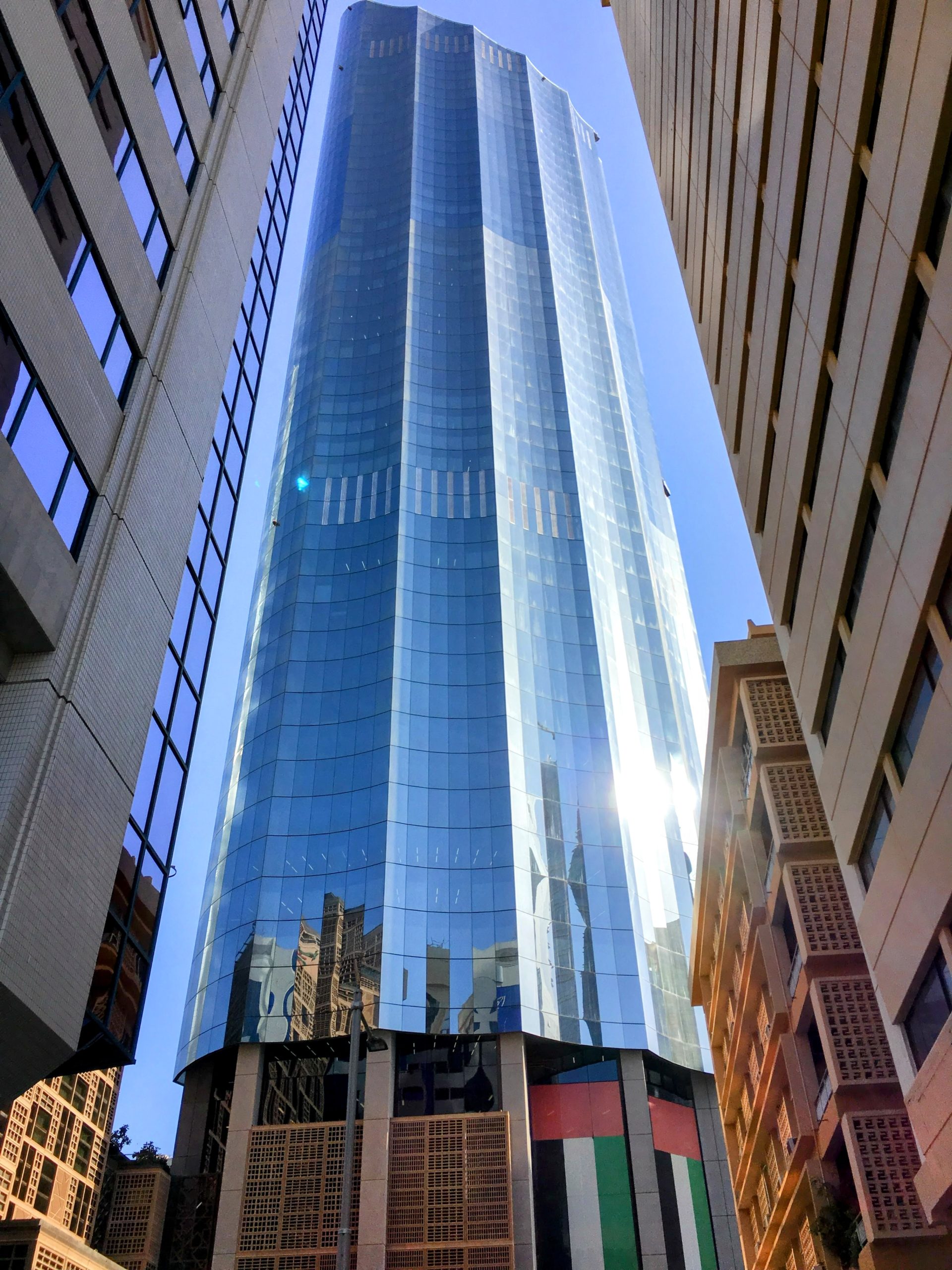 A tall modern glass building reflecting sunlight in the heart of Dubai surrounded by older architecture