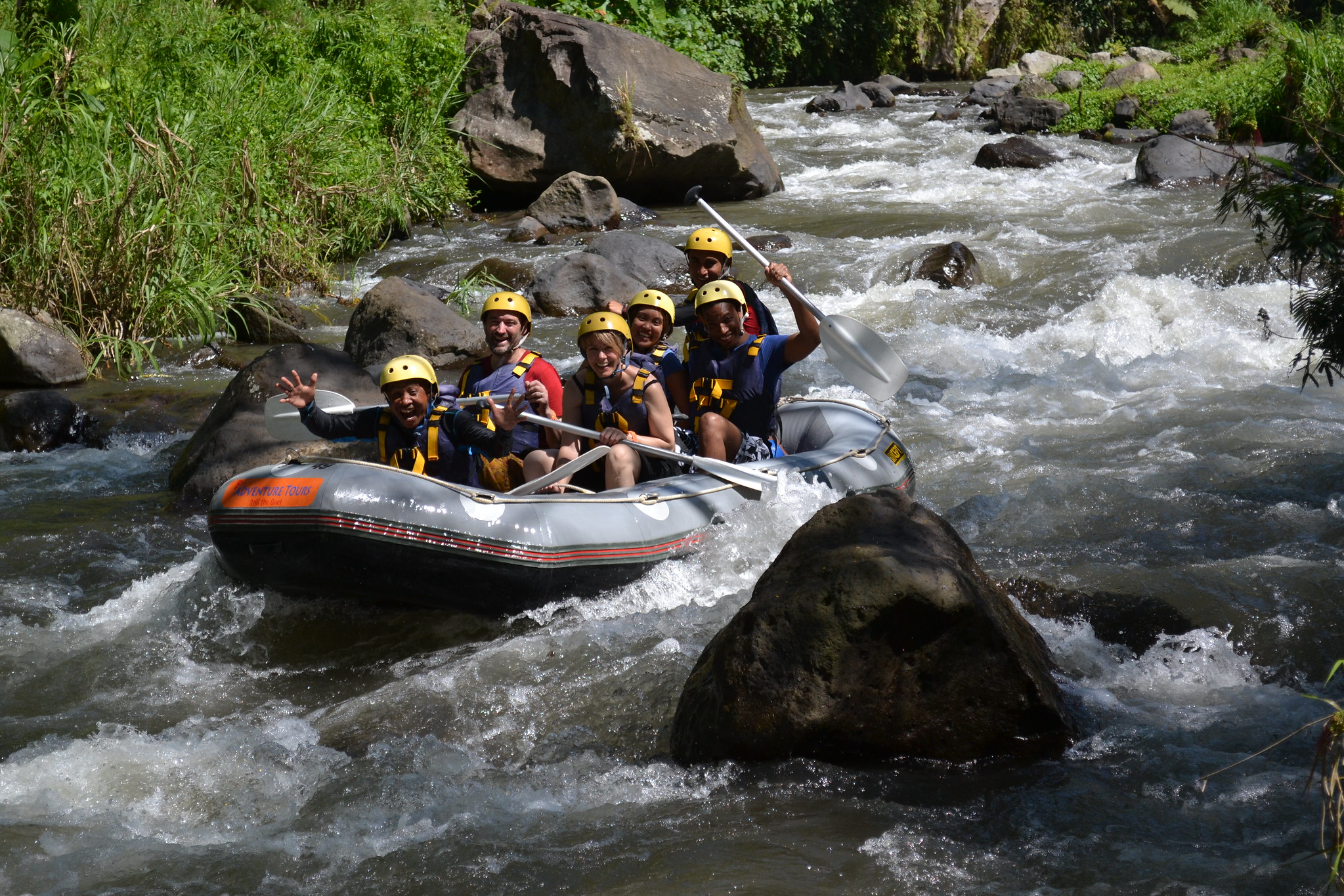 Students in helmets and life jackets raft through whitewater rapids on a river