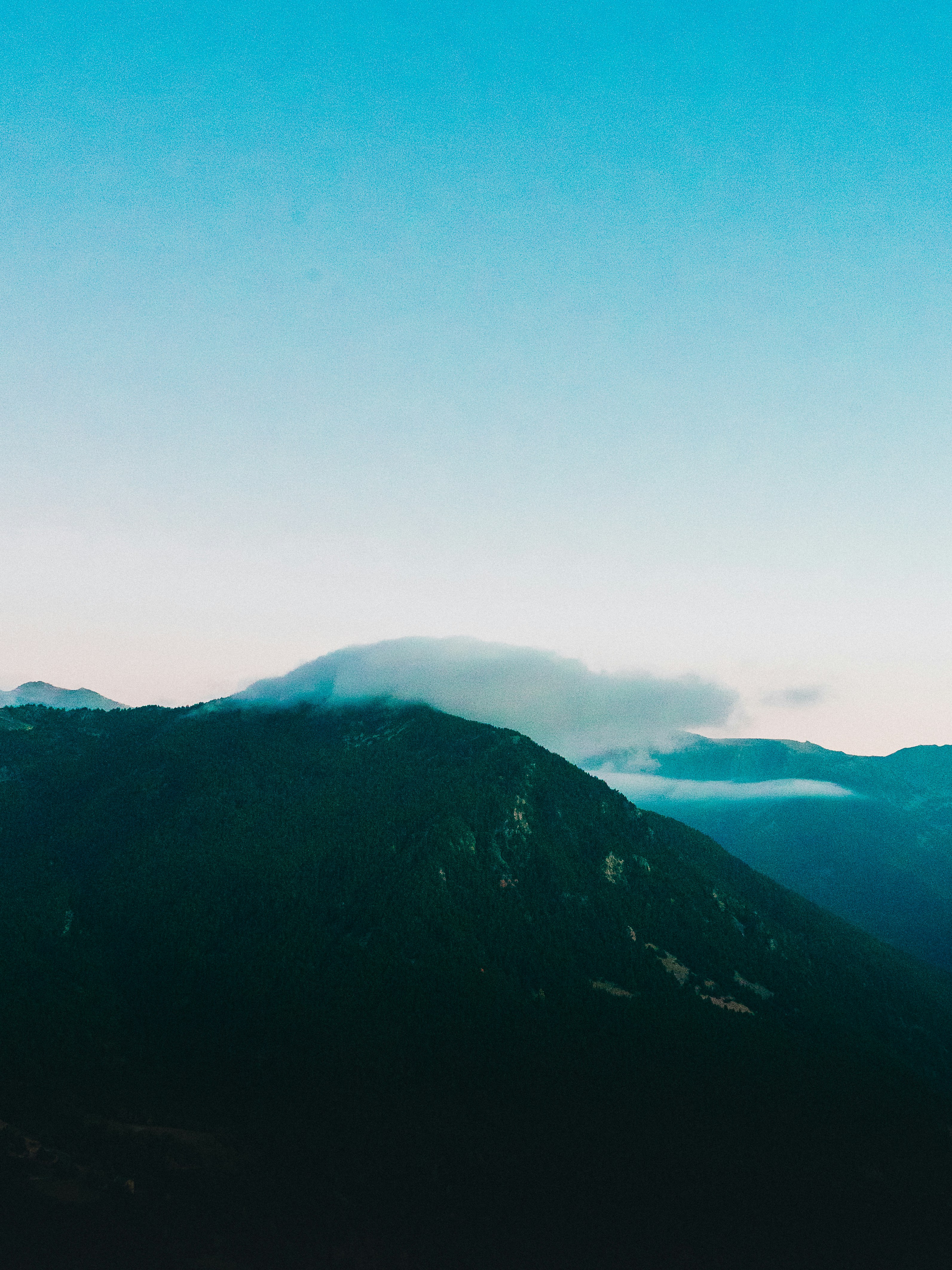 A dark mountain ridge silhouetted against a pale turquoise sky at dusk, low cloud along its crest.