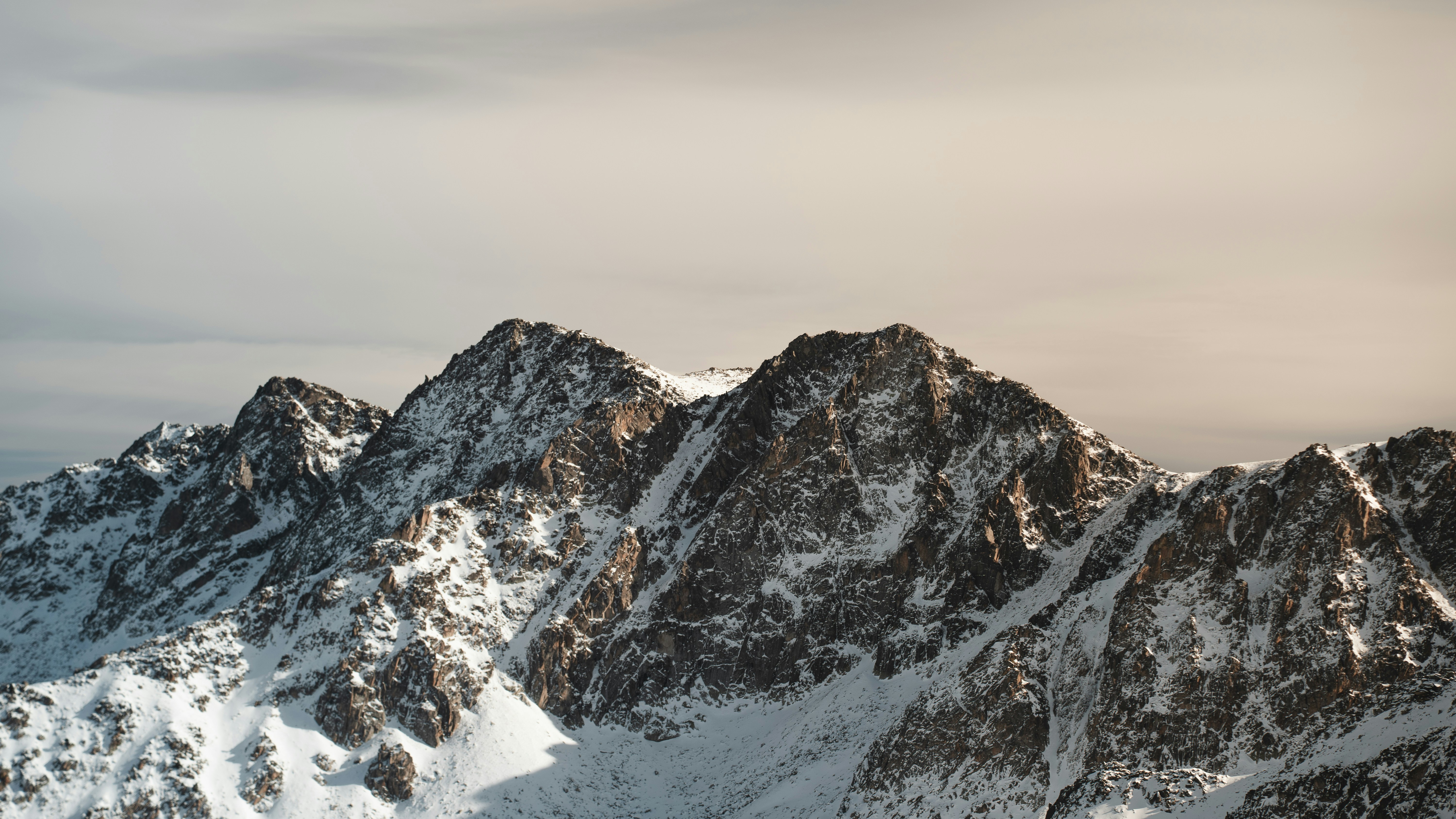 Bare rock summits streaked with snow under a pale overcast sky.