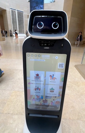 A robot with a face on top and a screen on its body, ready to help you navigate the museum.