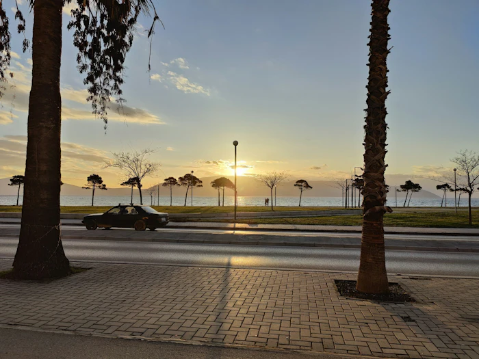 A palm-lined seafront promenade at sunset on the Albanian Riviera.