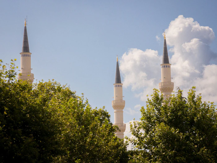 Three minarets rising above green trees against a blue sky.