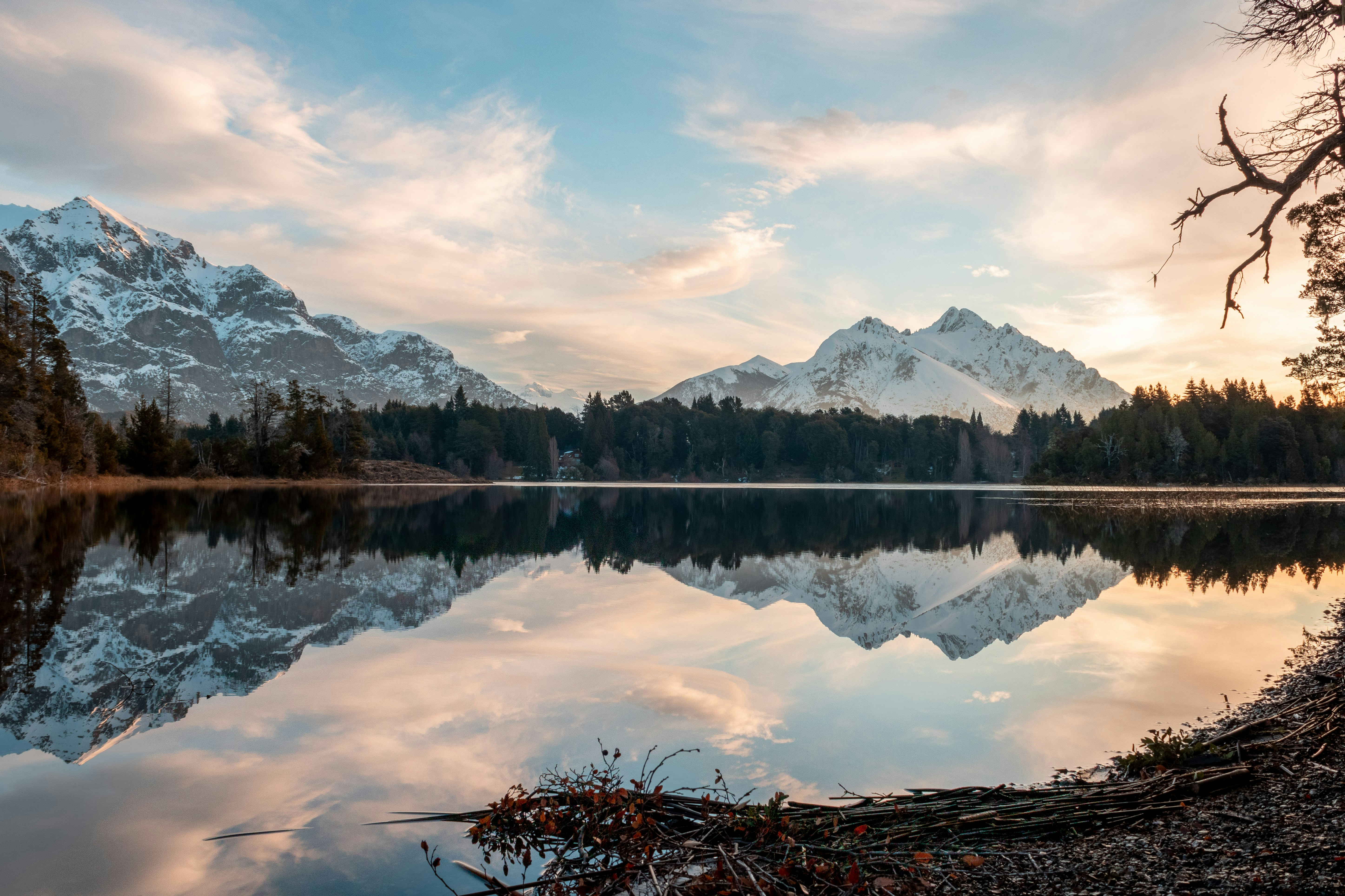 Snow-capped peaks and forest reflected in a still lake at dusk.