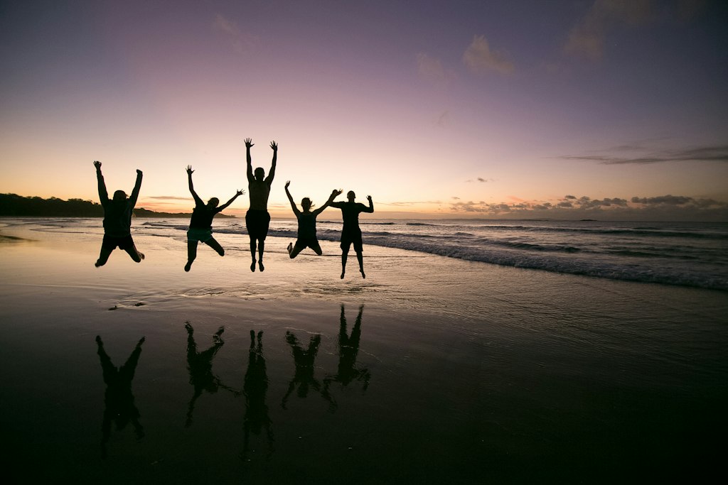 High school students jumping for joy at sunset on a beach in Australia during a Rustic Pathways student travel program
