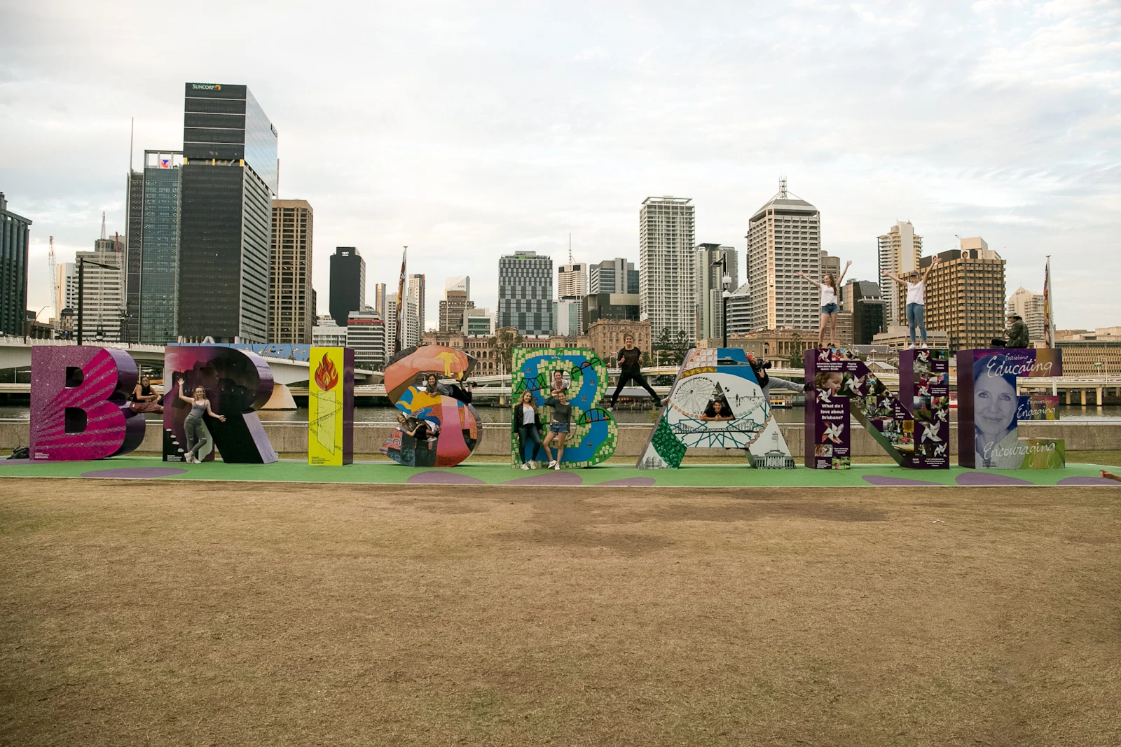 Large colorful letters spelling BRISBANE stand on a lawn in front of the city's towers