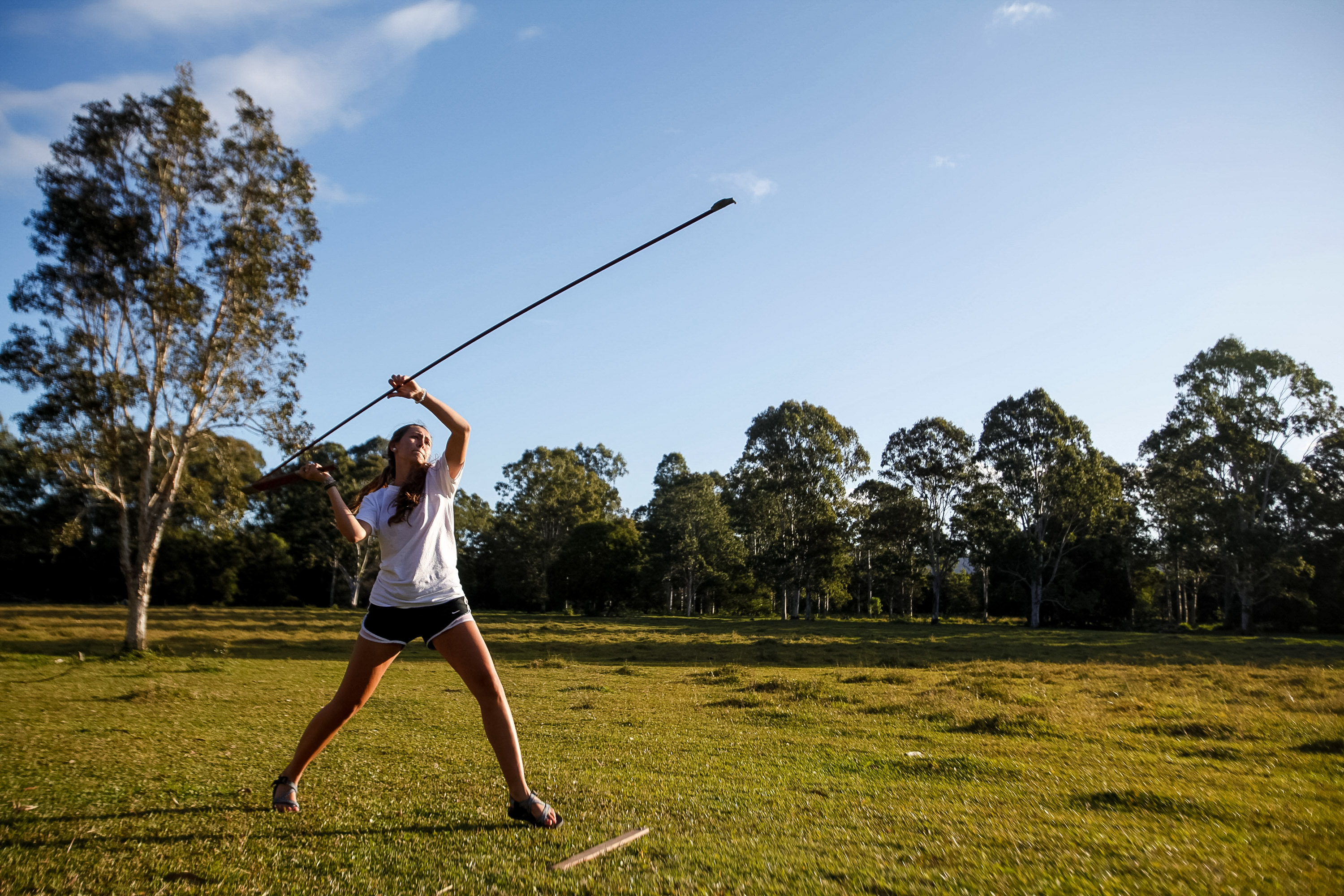 A student throws a javelin across a grassy field