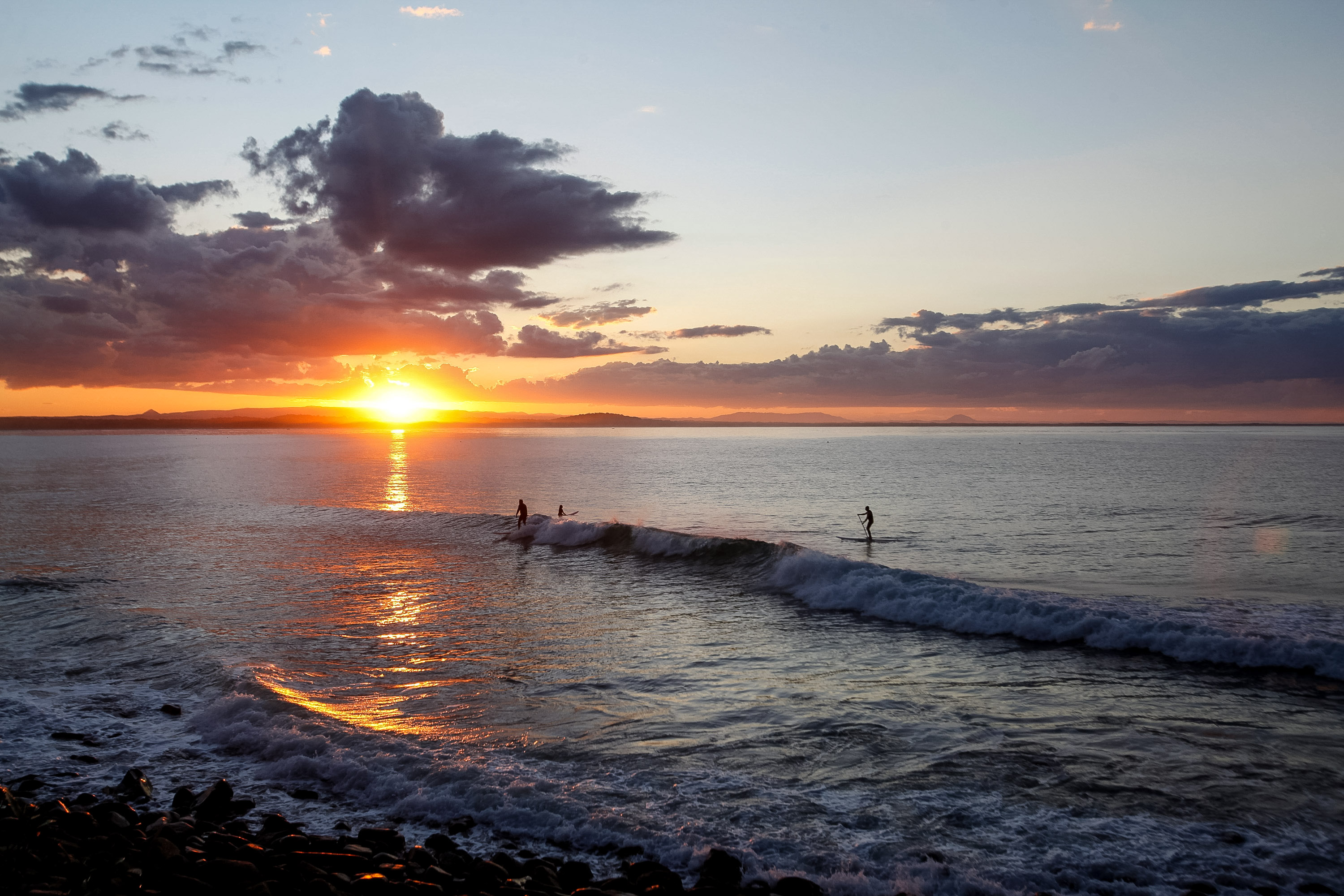 Surfers ride a wave as the sun sets over the ocean during a school trip