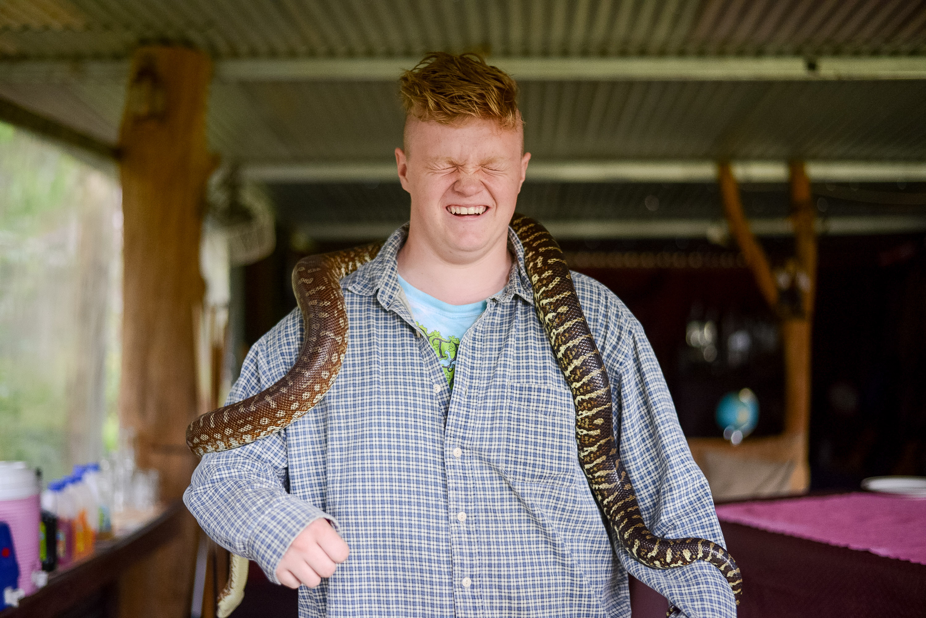 A student scrunches his face while holding a python draped over his shoulders