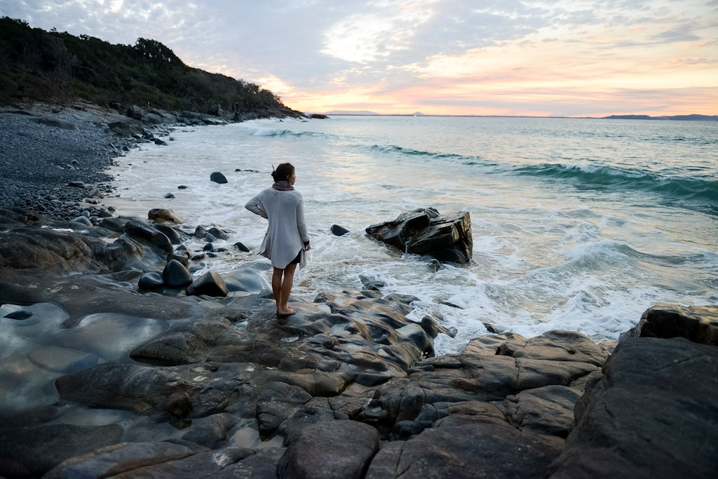 A woman standing on the edge of a coast looking into the sea.