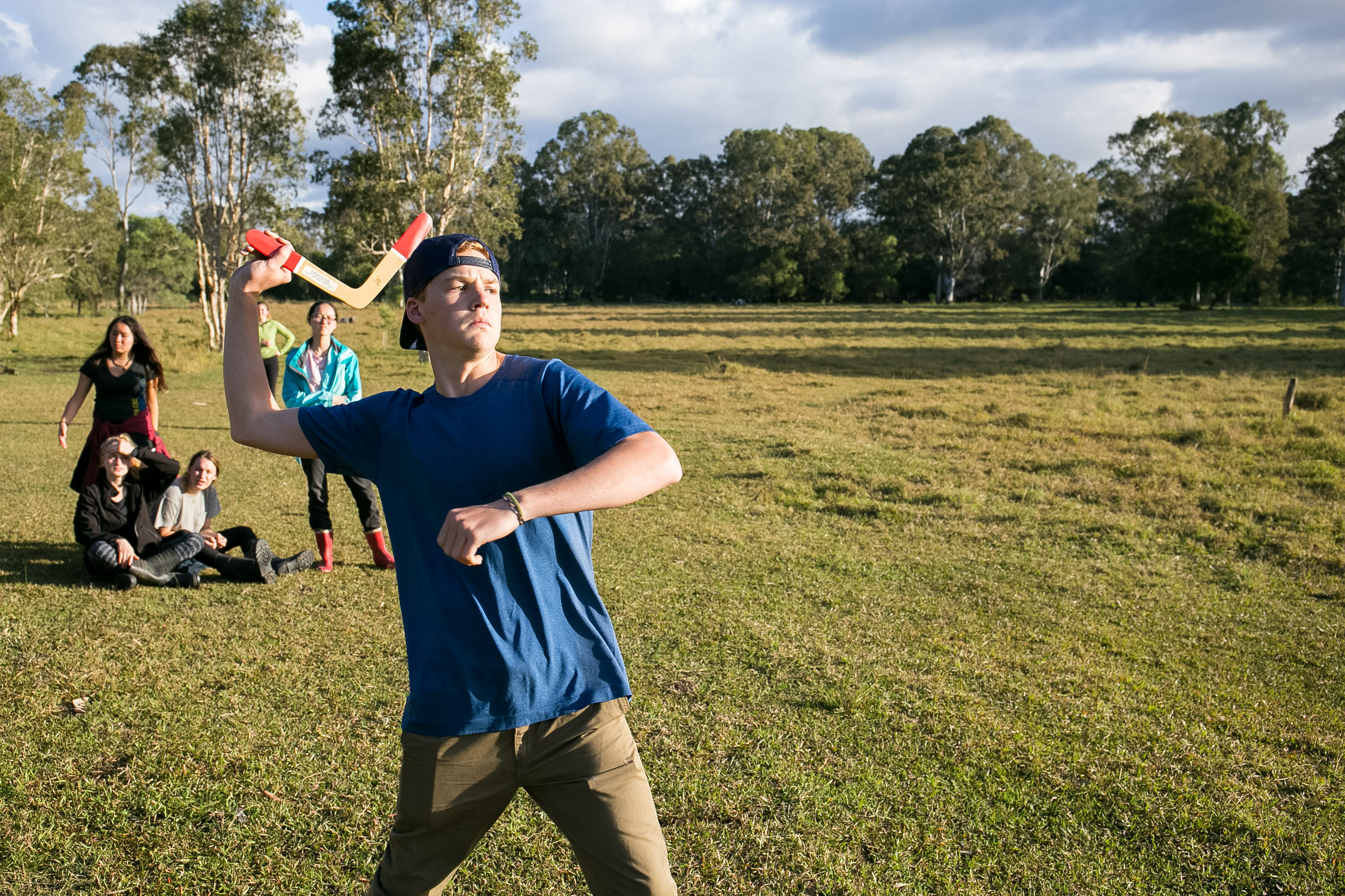 A student throws a boomerang in an open field in Australia while others watch nearby