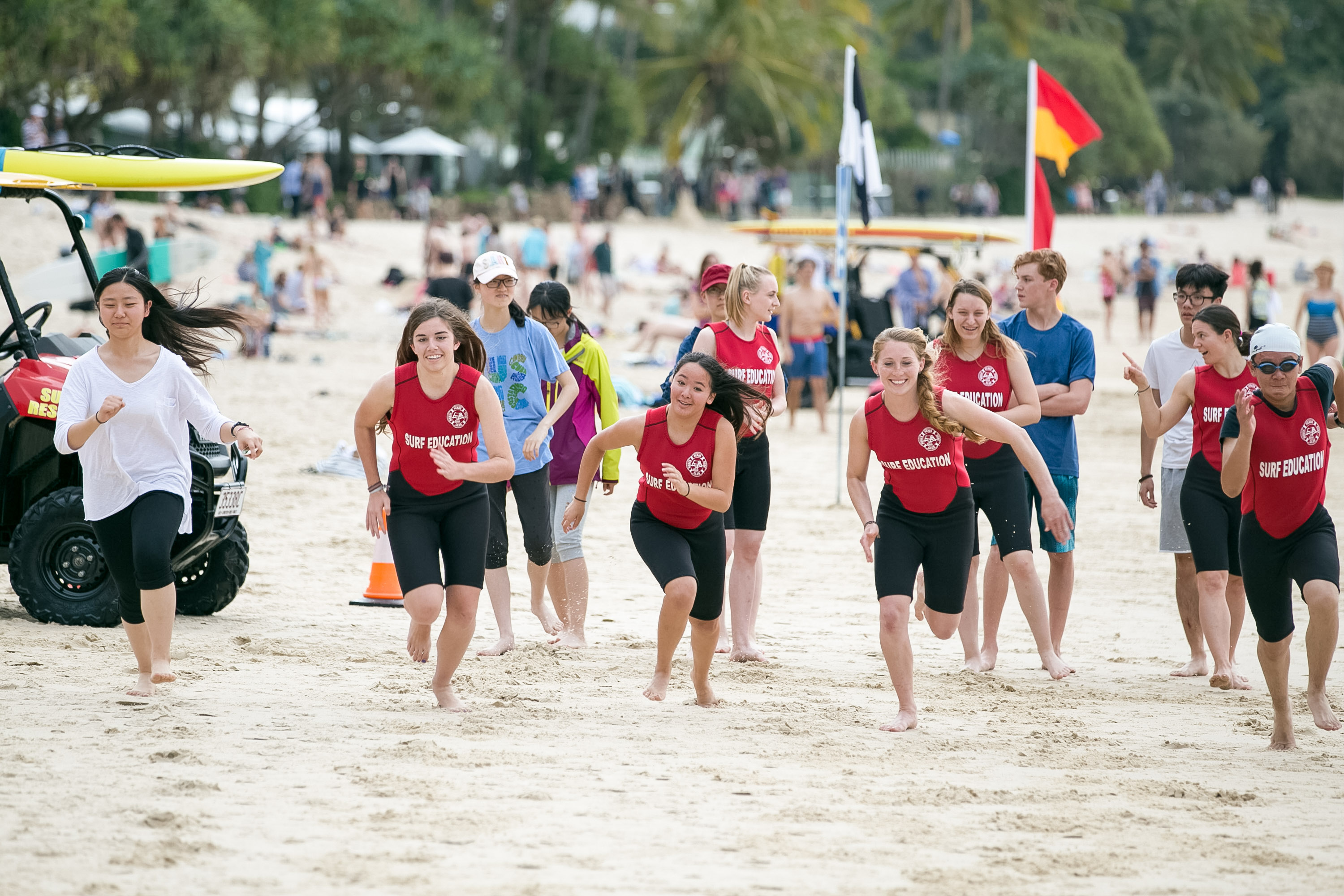 Students in red rash guards jog across the sand during a beach surf lifesaving drill