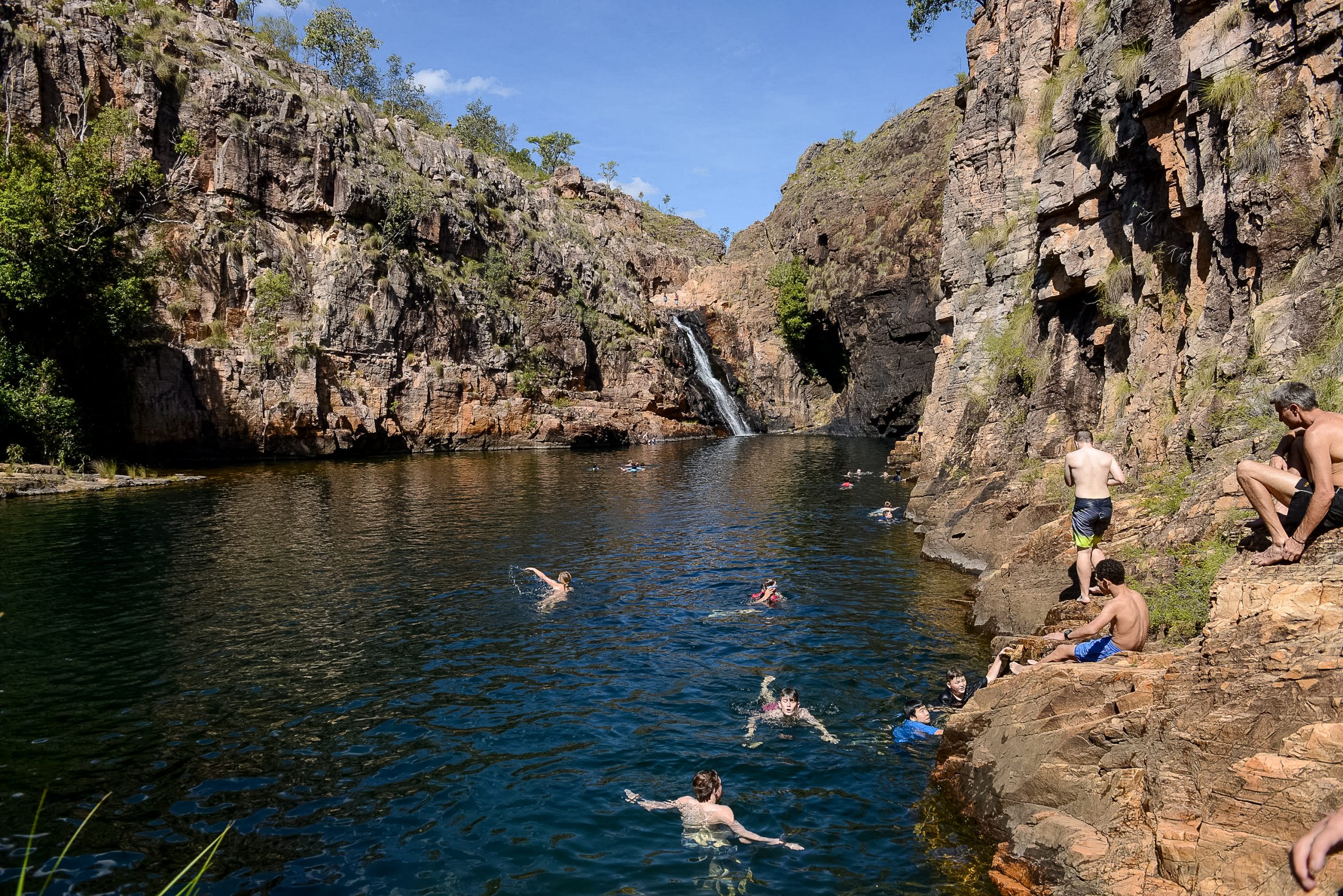 Students swim in a rock pool beneath a waterfall in a sandstone gorge in Australia