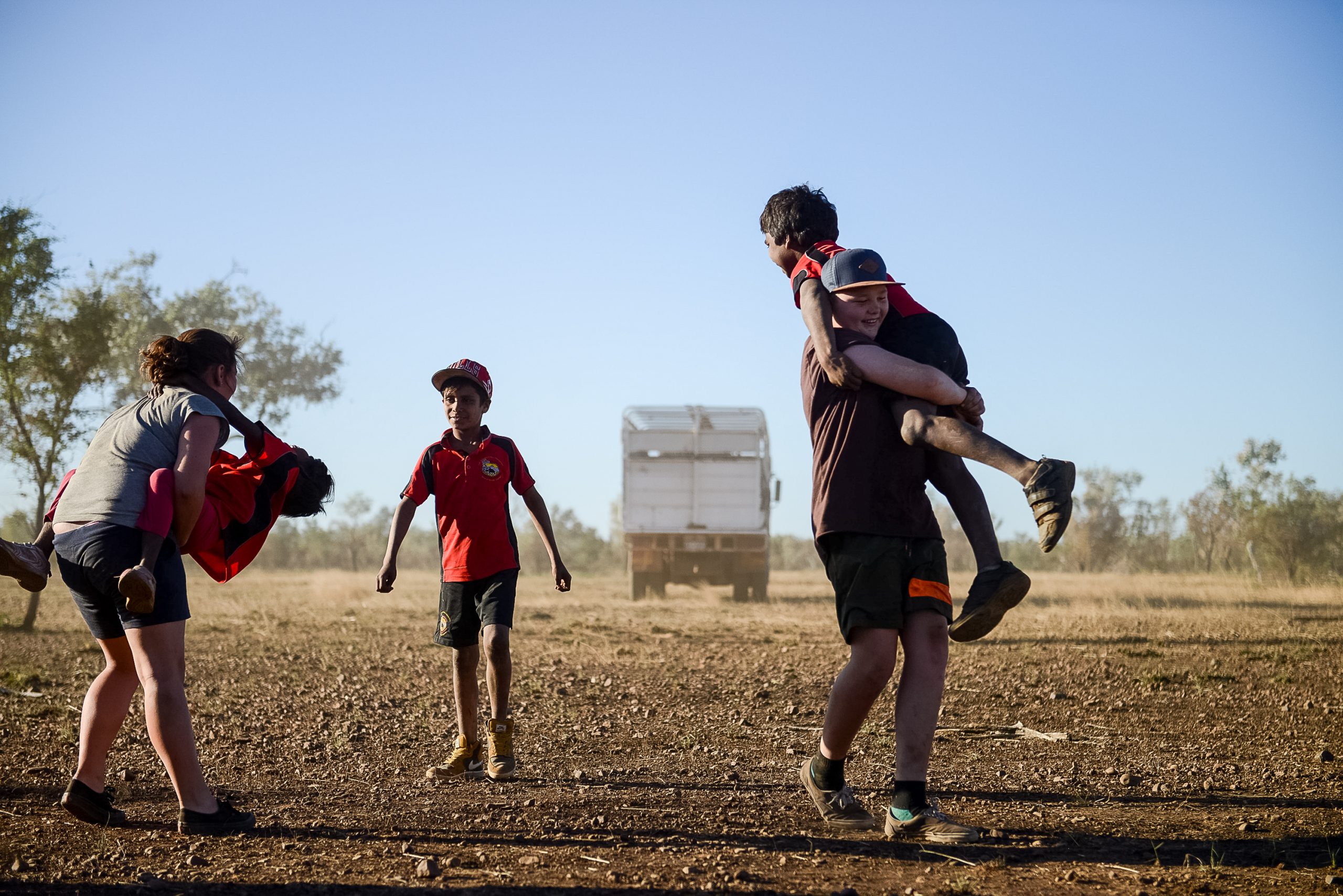 A student carries a friend piggyback across a dusty outback field in Australia