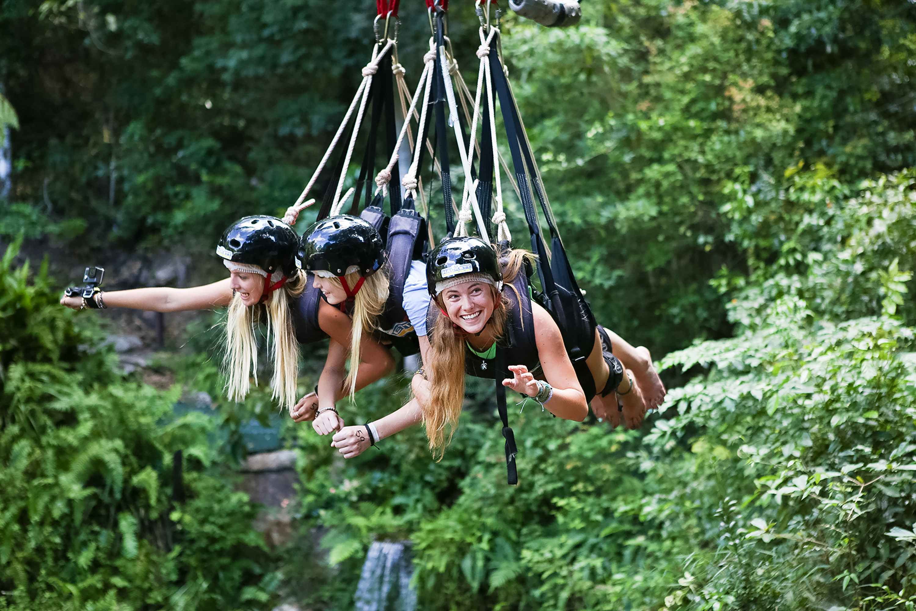 Students in helmets soar through the rainforest canopy on a zipline swing