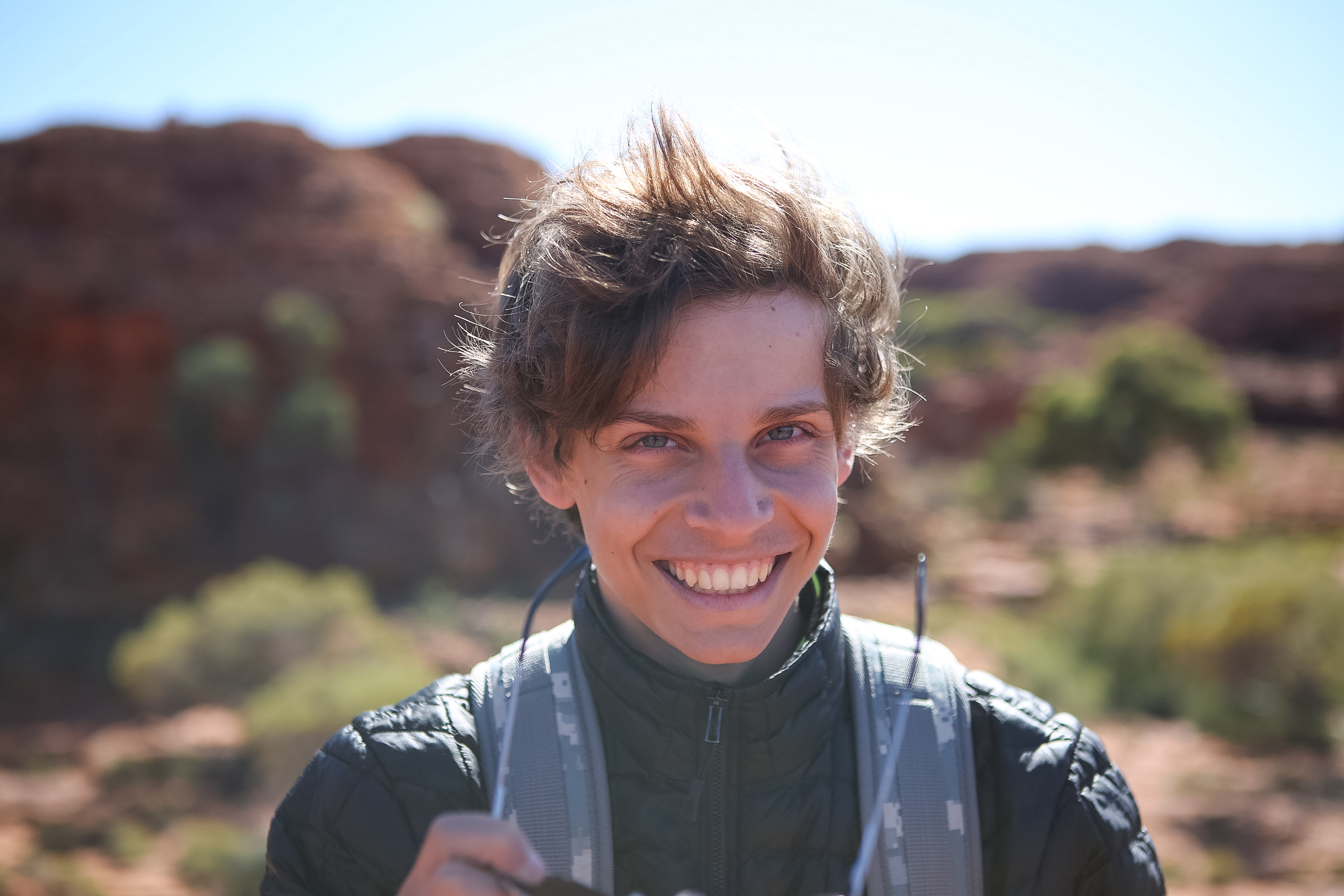 A student smiles for the camera against a red-rock outback landscape