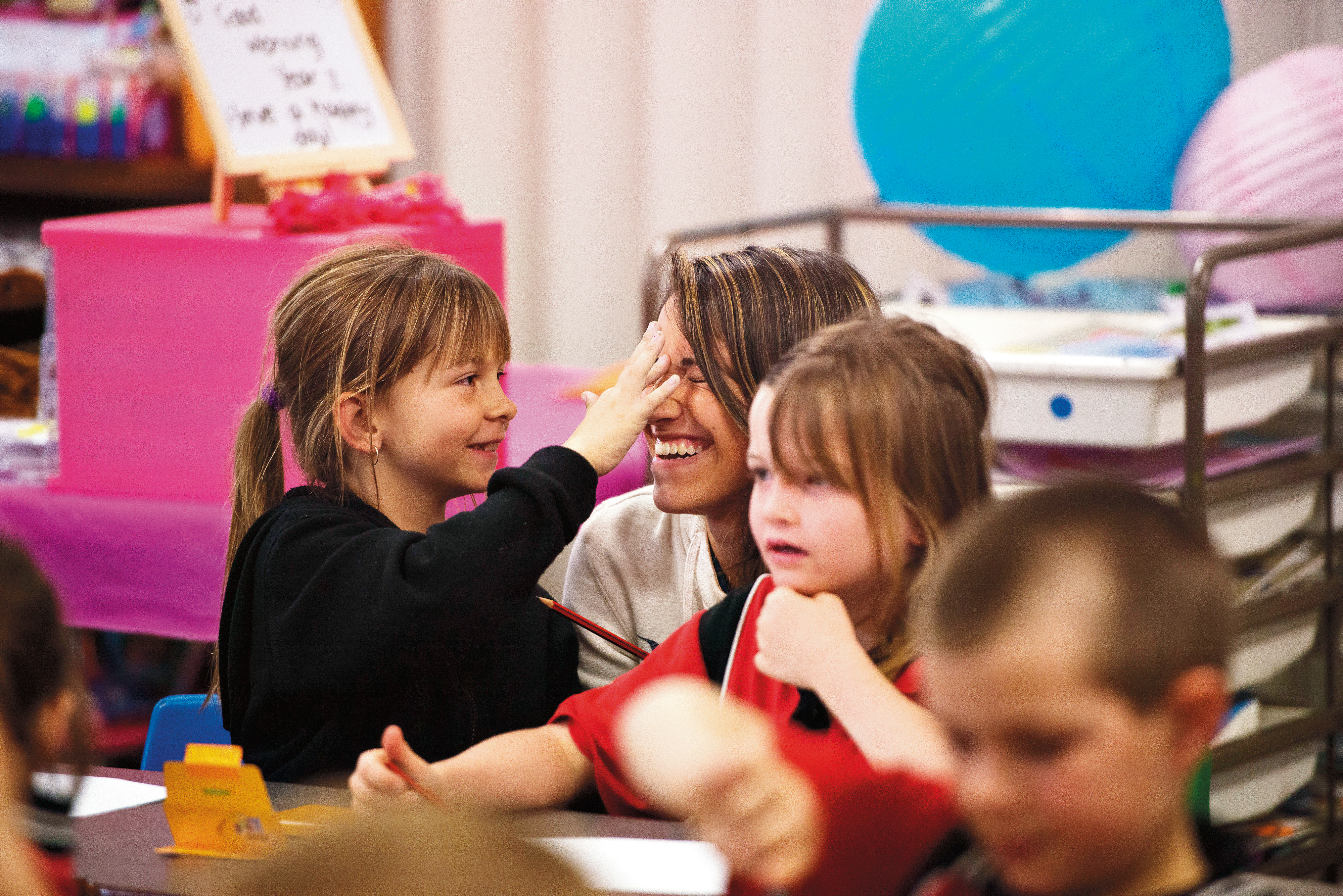 A student answers a question at a classroom desk beside primary school children