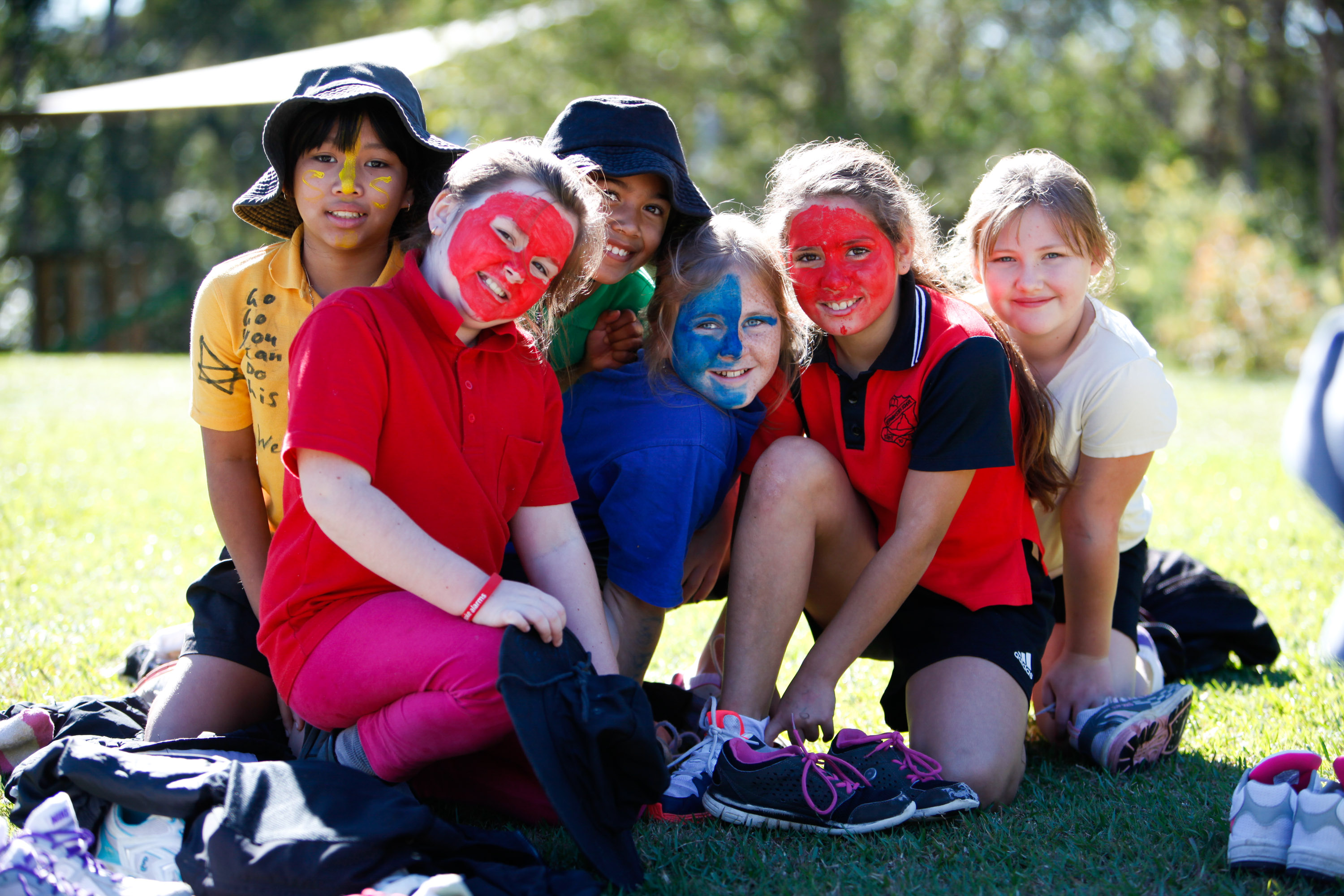 Students with painted faces kneel together on grass outdoors