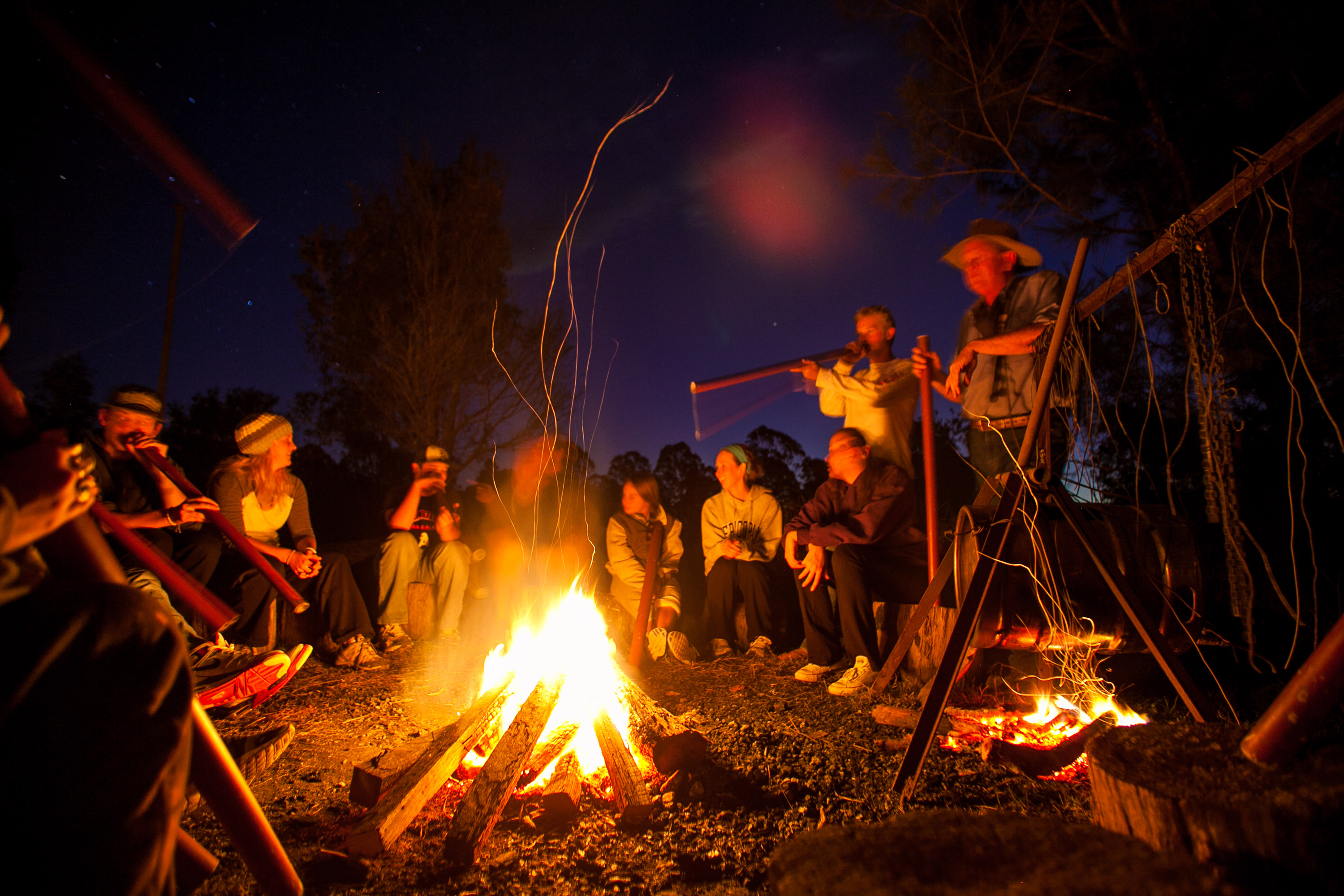 Firelight catches students seated in a circle at a bush camp after dark