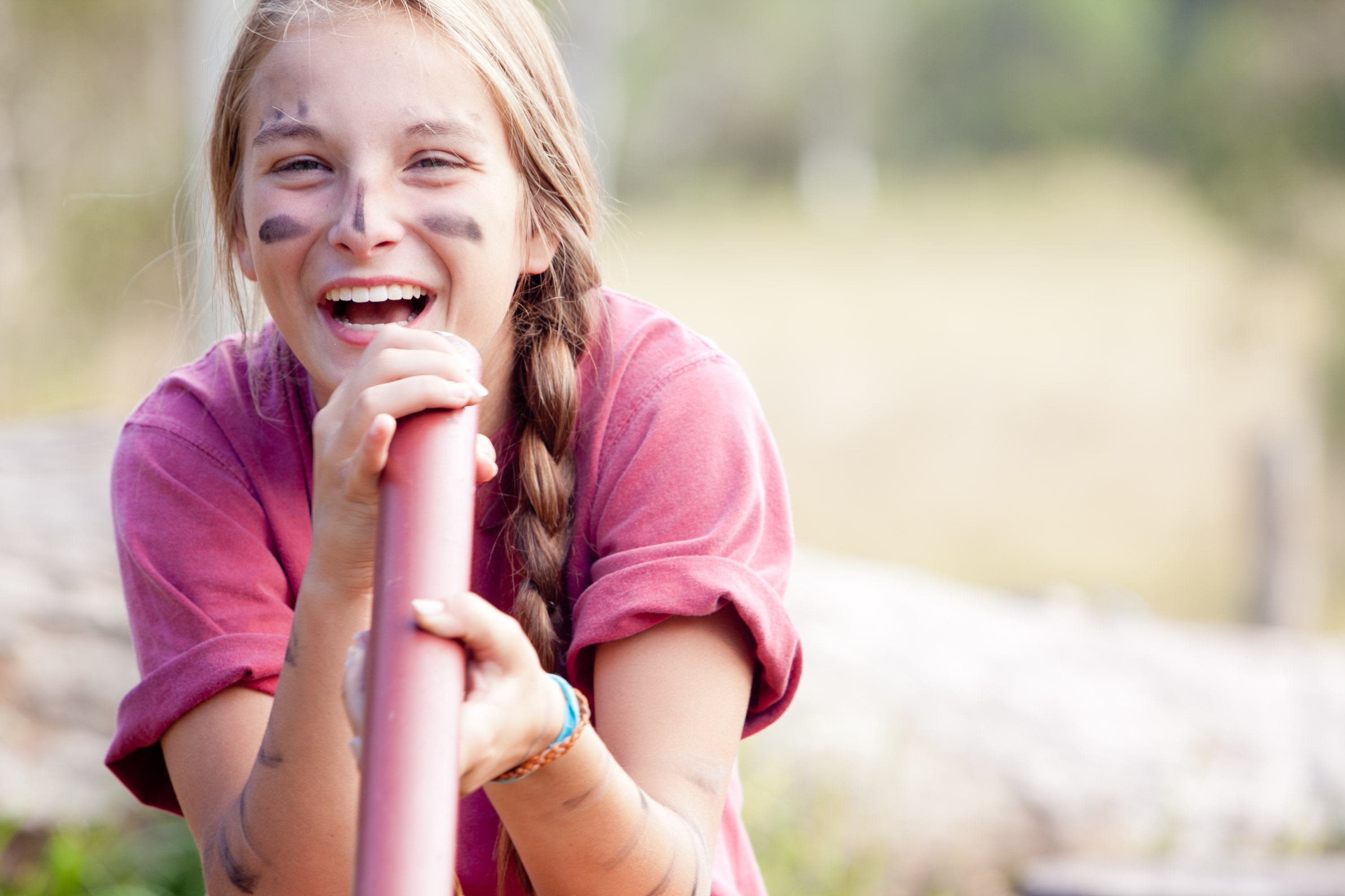 A student with painted face markings laughs while gripping a pole