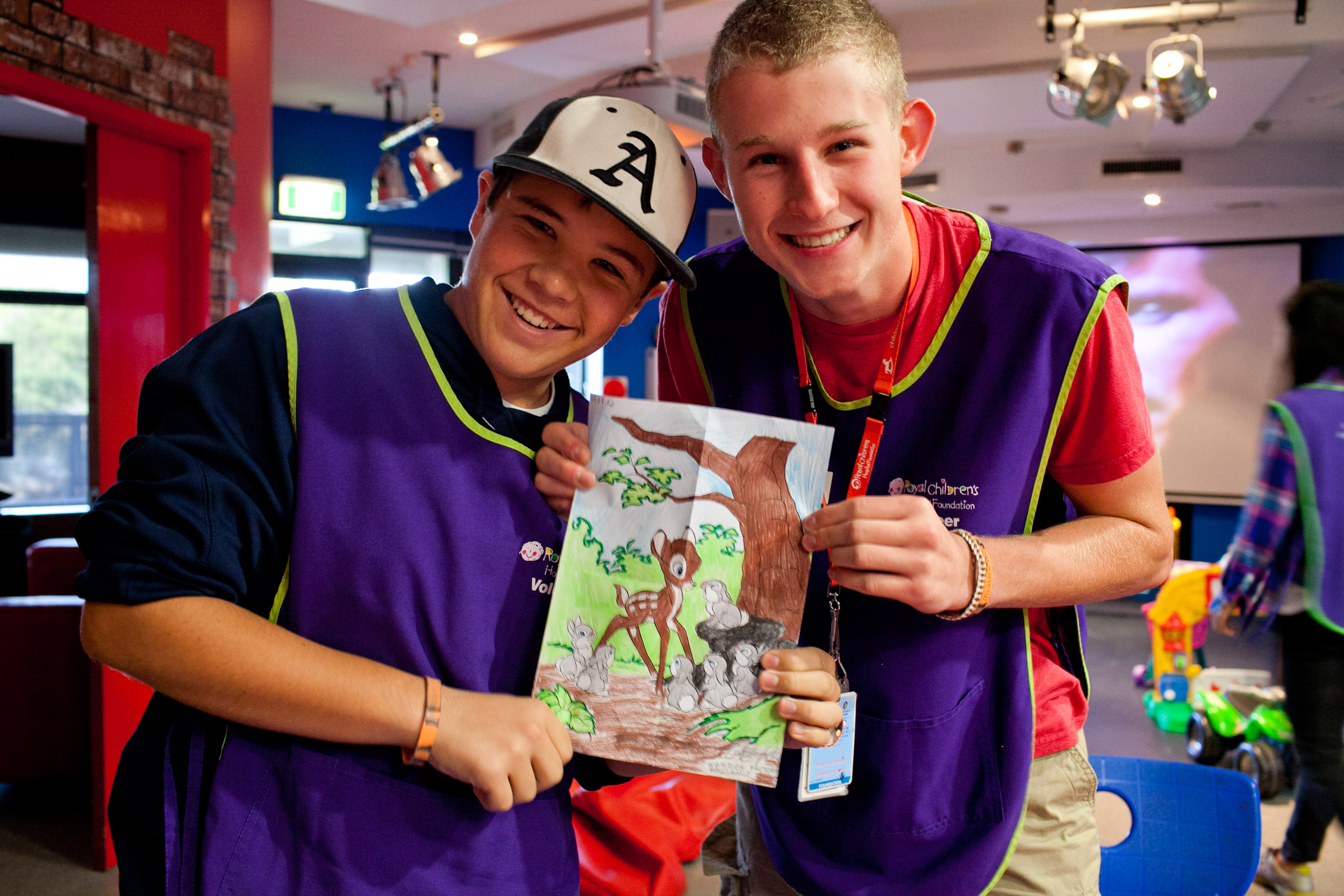 Students smile while holding up a hand-drawn picture during a craft activity