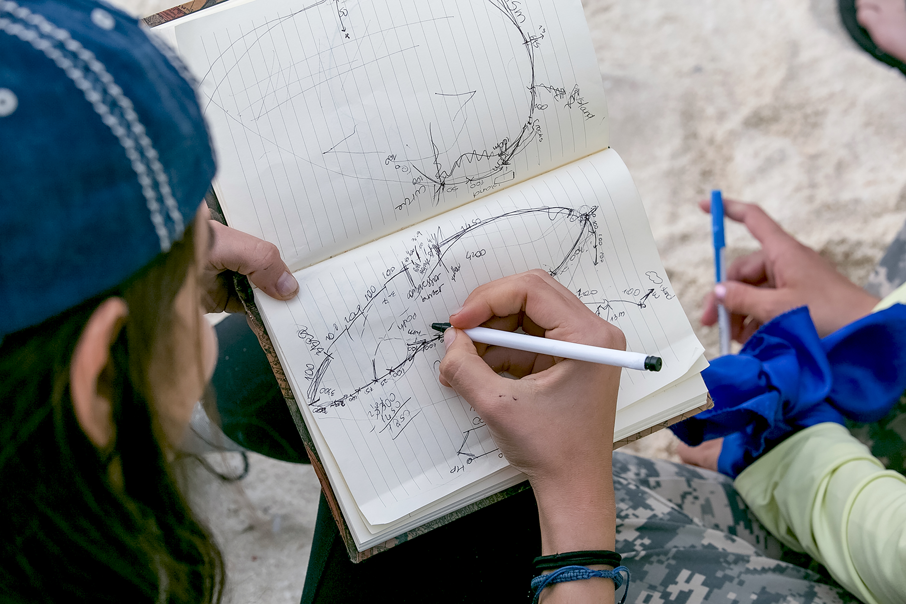 A student sketches a diagram in a lined notebook, pen in hand