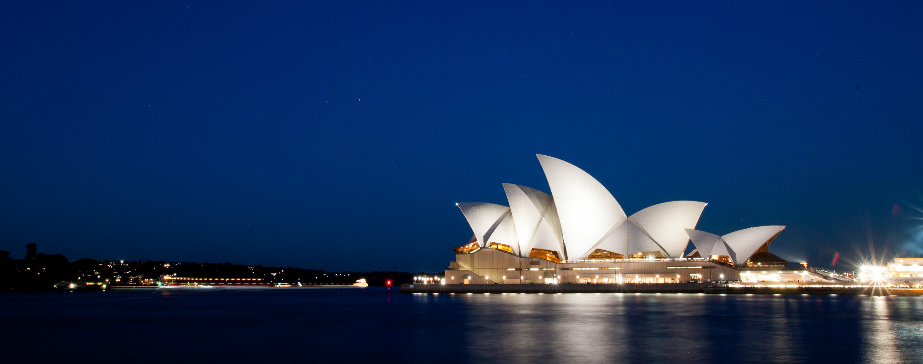 The Sydney Opera House and Harbour Bridge at dusk across still water