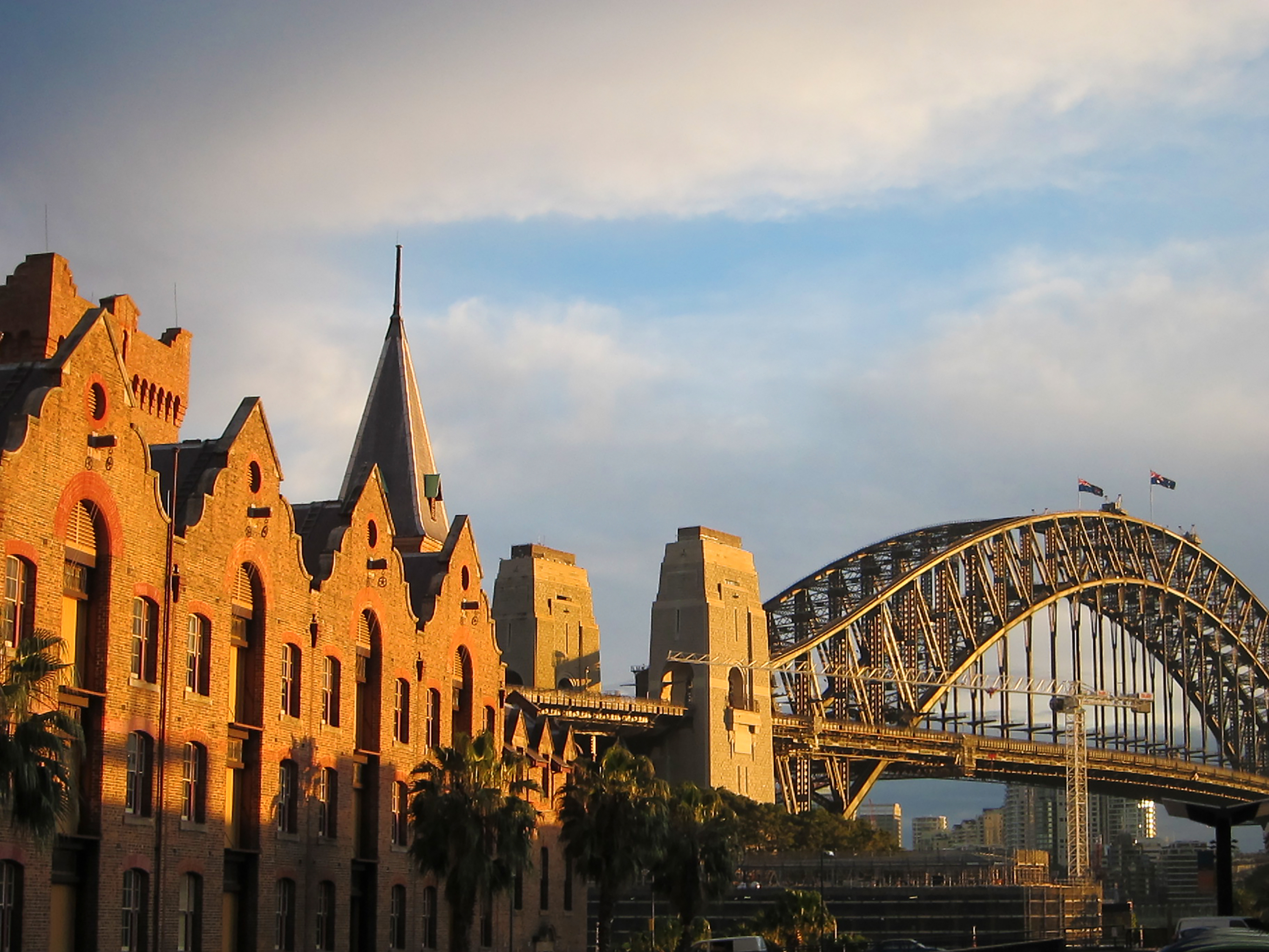 The Sydney Harbour Bridge rises behind historic sandstone warehouses at golden hour