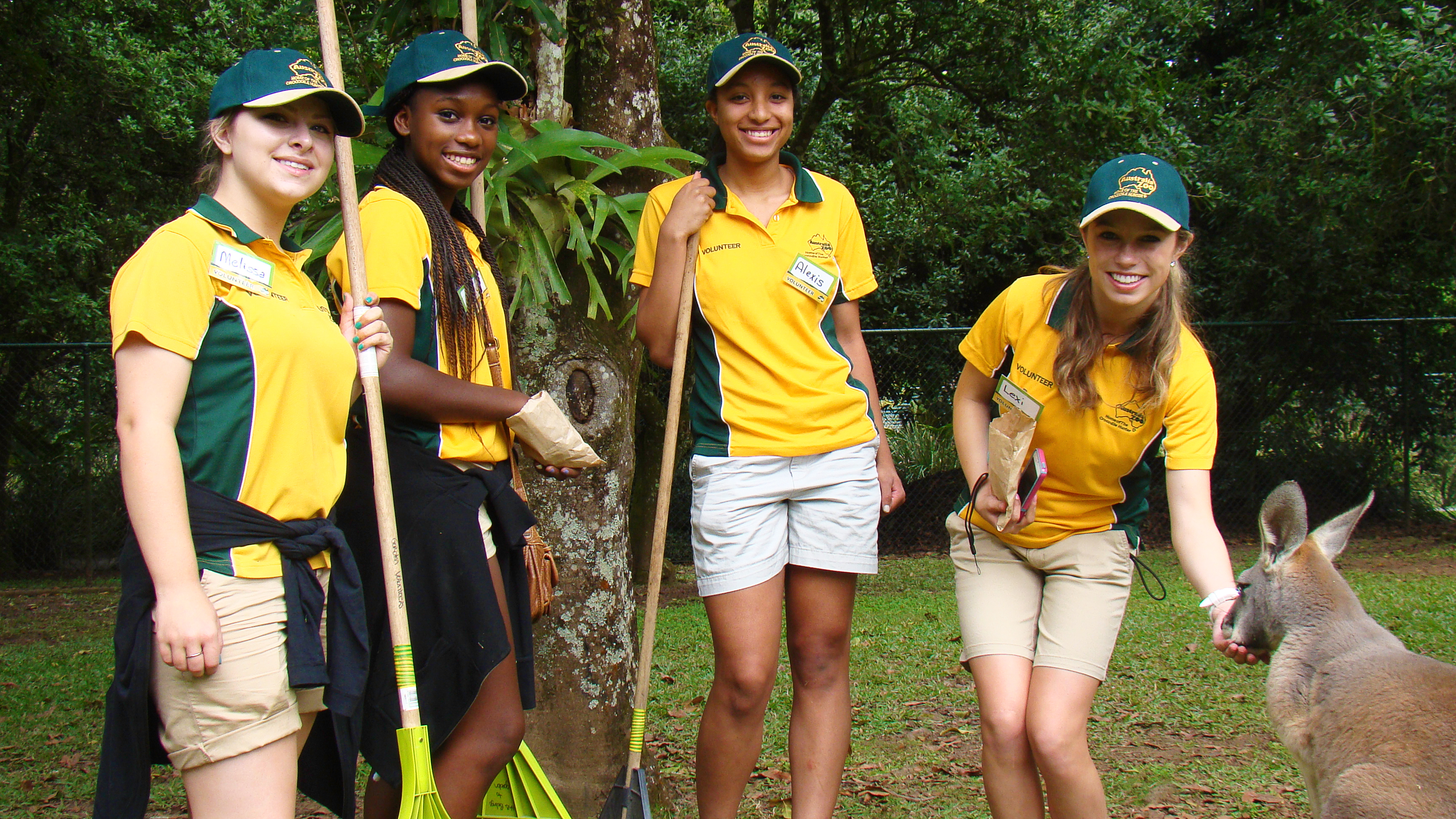 Students in matching zoo uniforms pose with cleaning tools beside a kangaroo