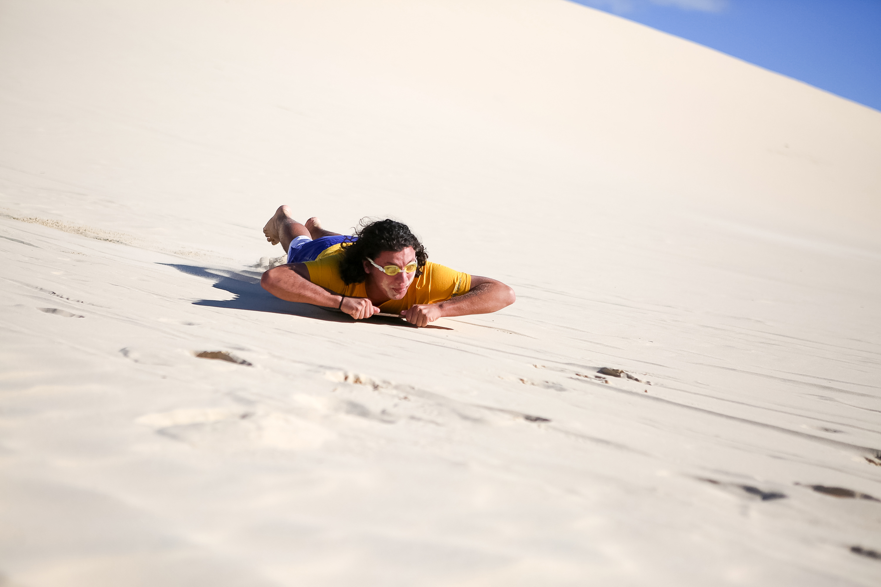 A student slides down a sand dune on their stomach