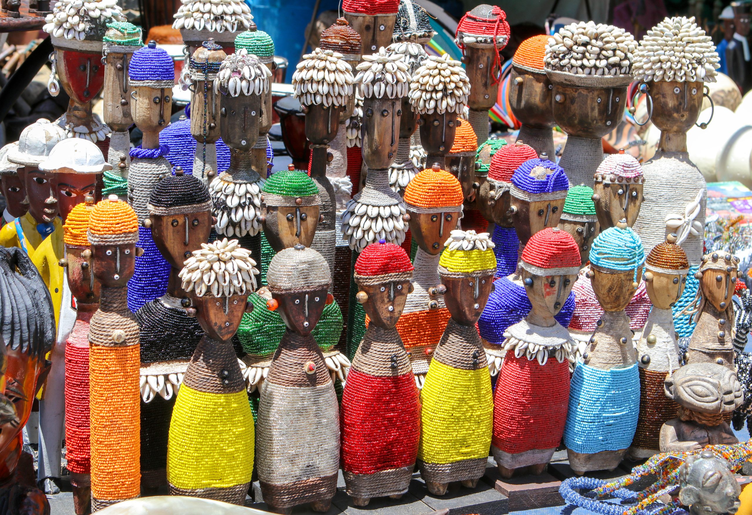 Rows of beaded wooden figurines with shell headdresses displayed at a market stall