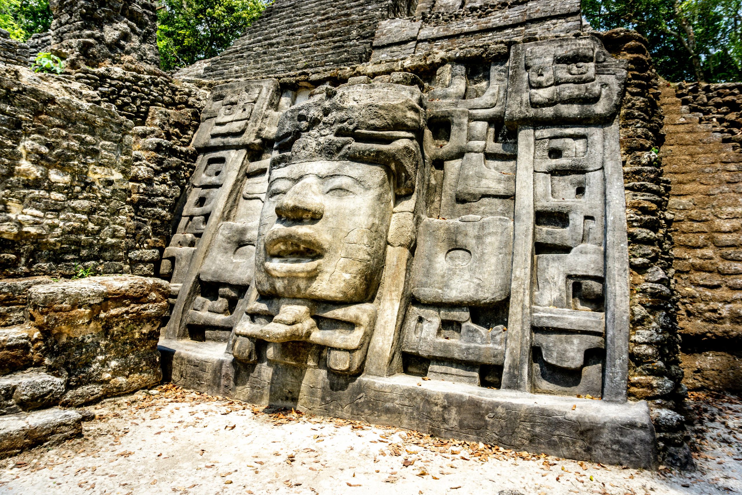 A carved stone Maya mask decorates the stone facade of an ancient ruin