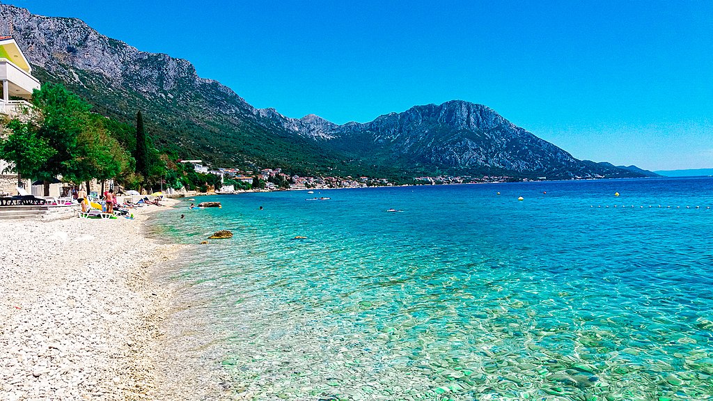 Turquoise water and pebble beach line the Croatian coast beneath rocky mountains
