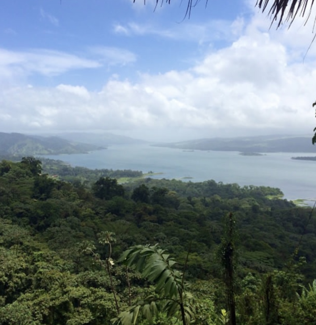Scenic view of a lake surrounded by green hills and cloudy sky.