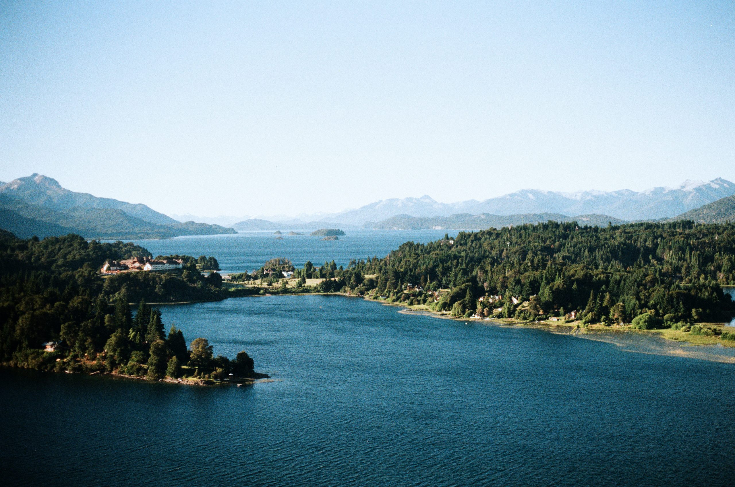 Student travelers pause where a forested lake winds between mountains under a clear sky in Patagonia