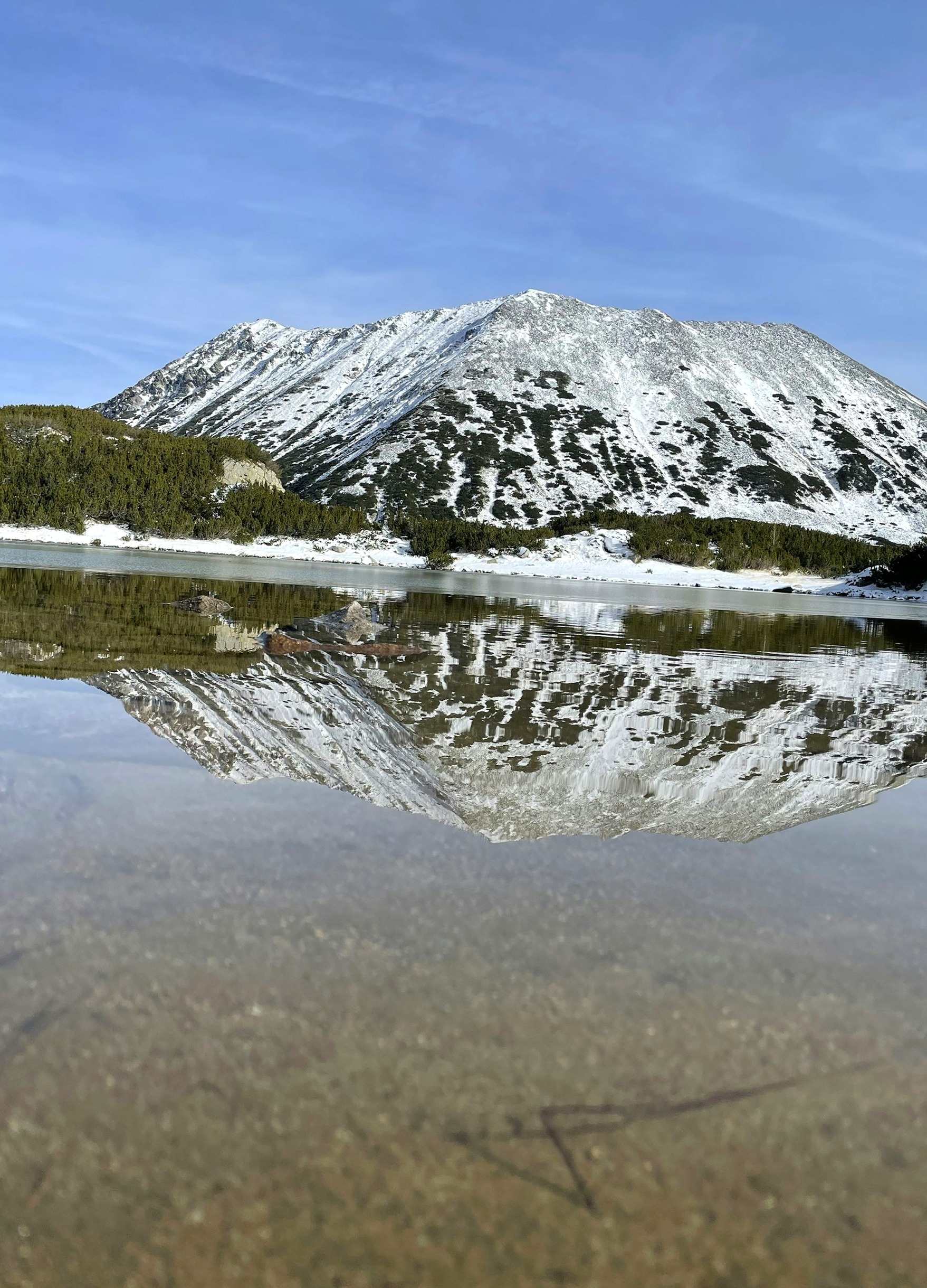 A snow-streaked peak of the Pirin range reflected in a still mountain lake.