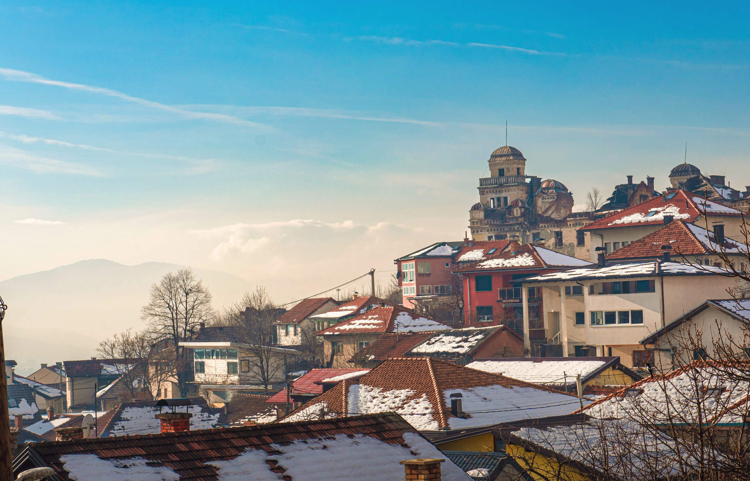 Snow lying on the rooftops of Sarajevo, with a large building standing on the ridge above the city.