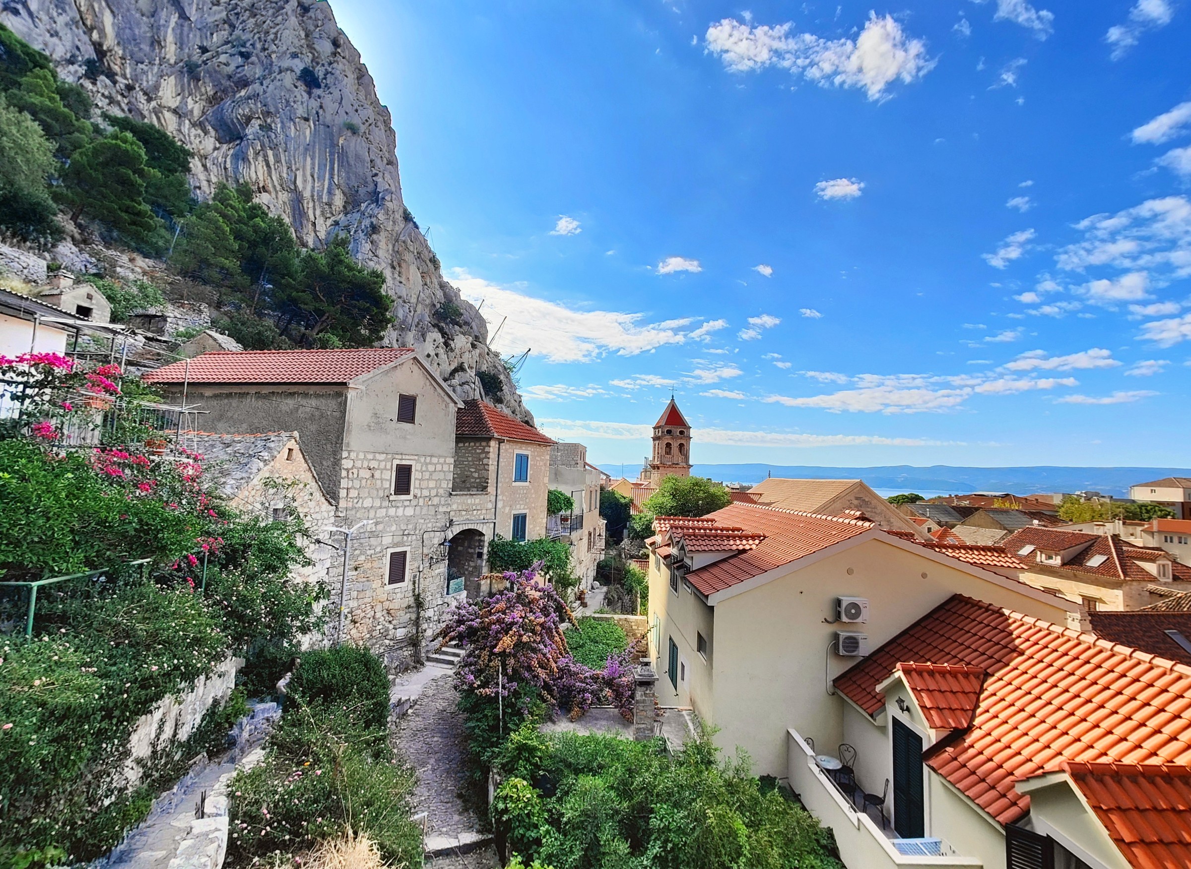Red-roofed houses and a church tower below a limestone cliff on the Bay of Kotor in Montenegro, with the water beyond.