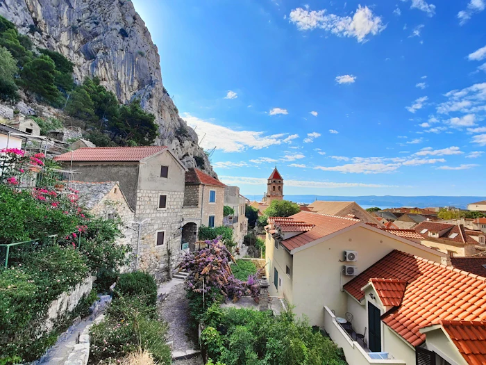 Red-roofed houses and a church tower below a limestone cliff on the Bay of Kotor in Montenegro, with the water beyond.