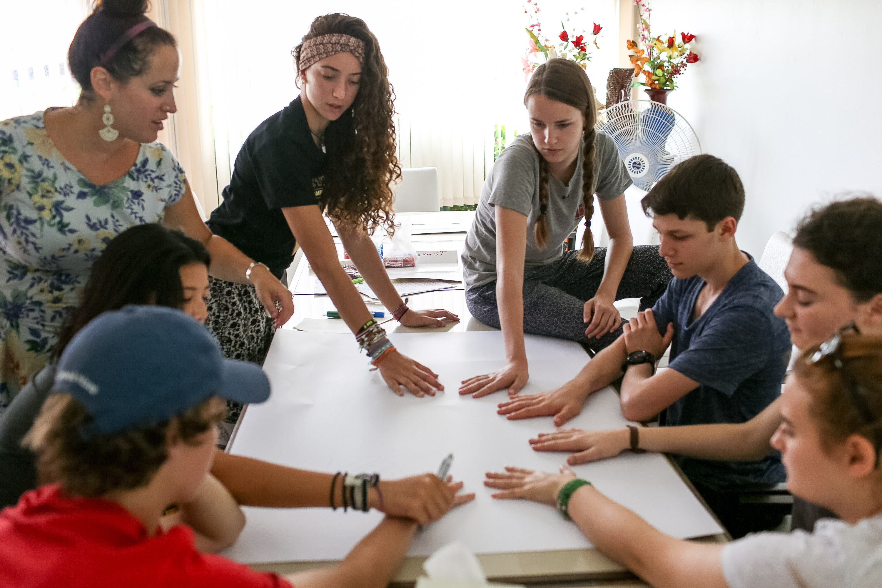 Students and a leader gather around a large sheet of paper on a table during a group activity